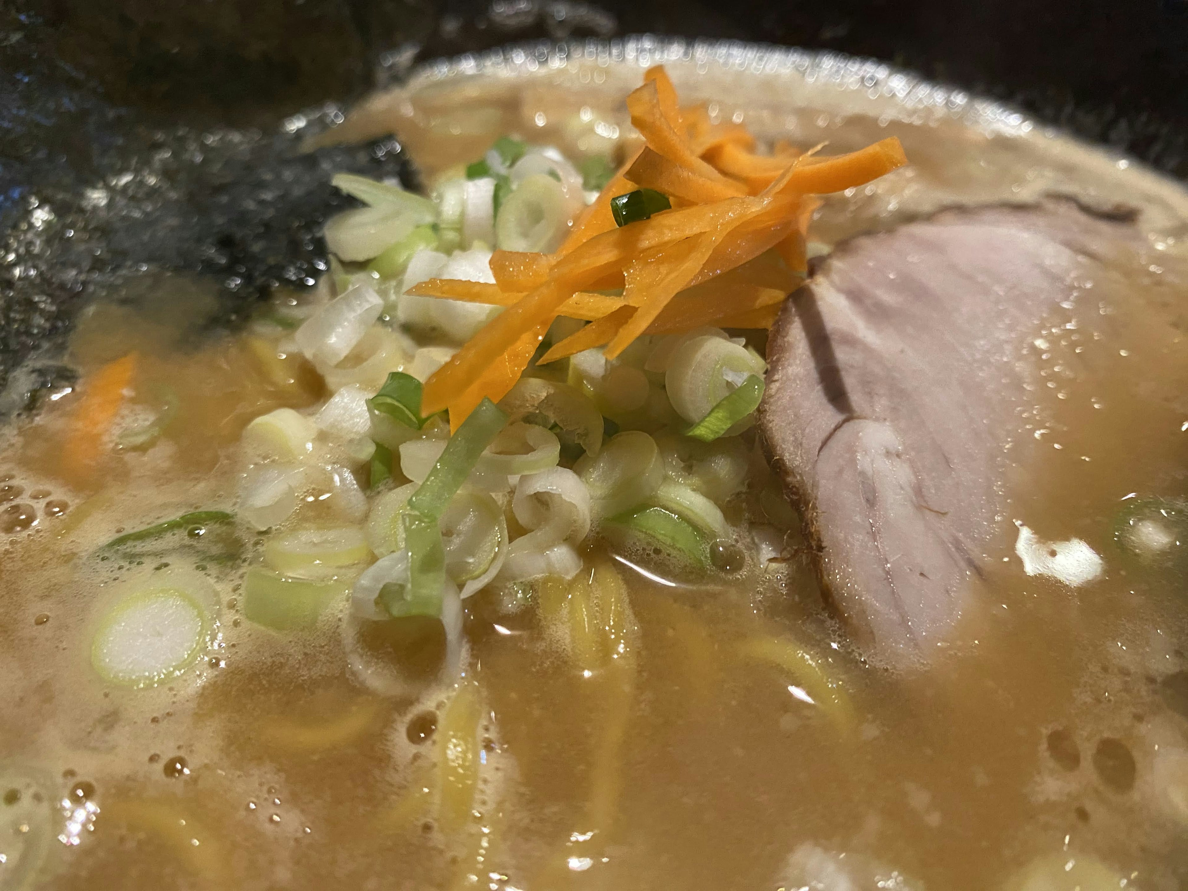 Close-up of ramen with green onions and shredded carrots in broth