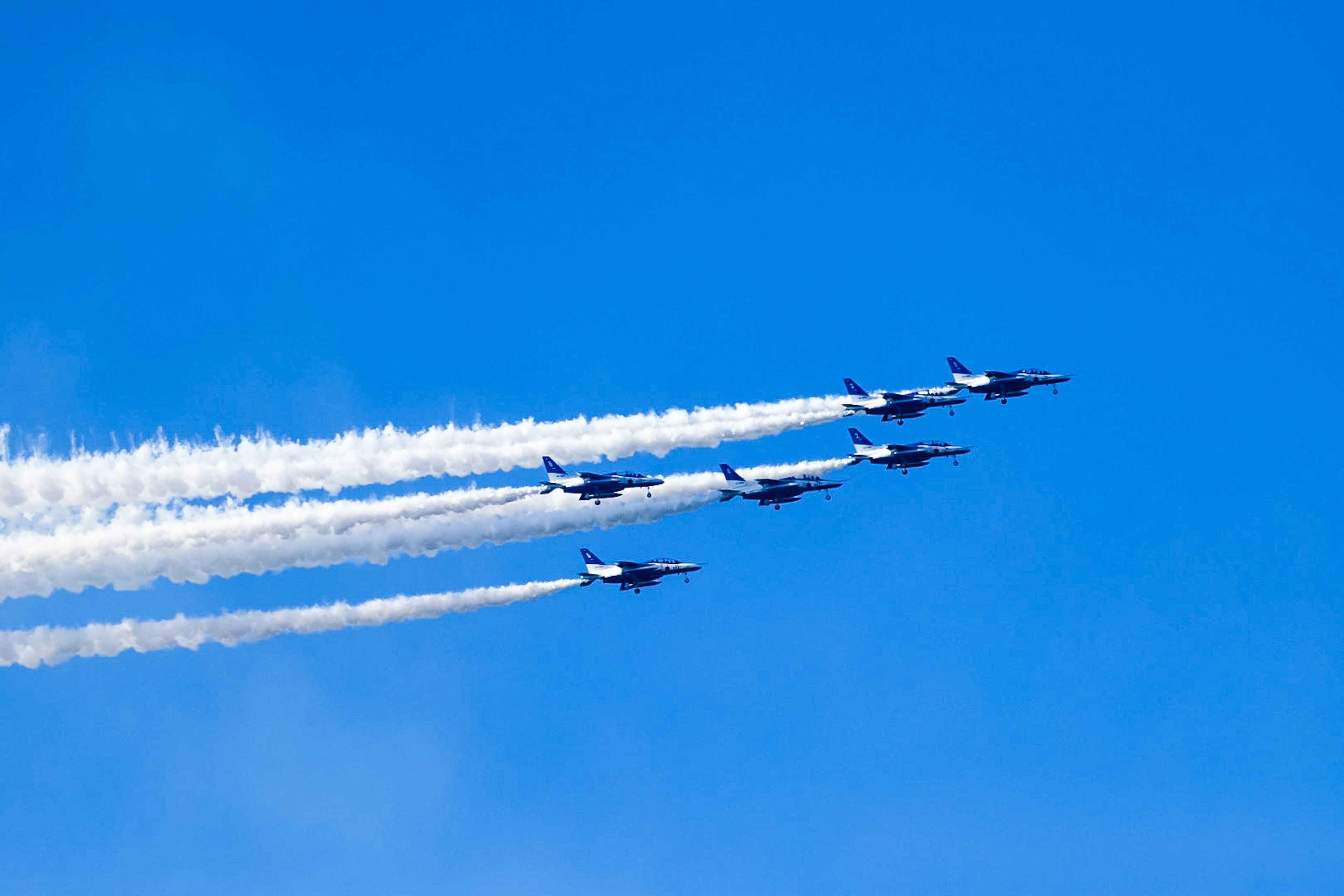 Sei jet da combattimento in volo in formazione nel cielo blu con scie di vapore bianche