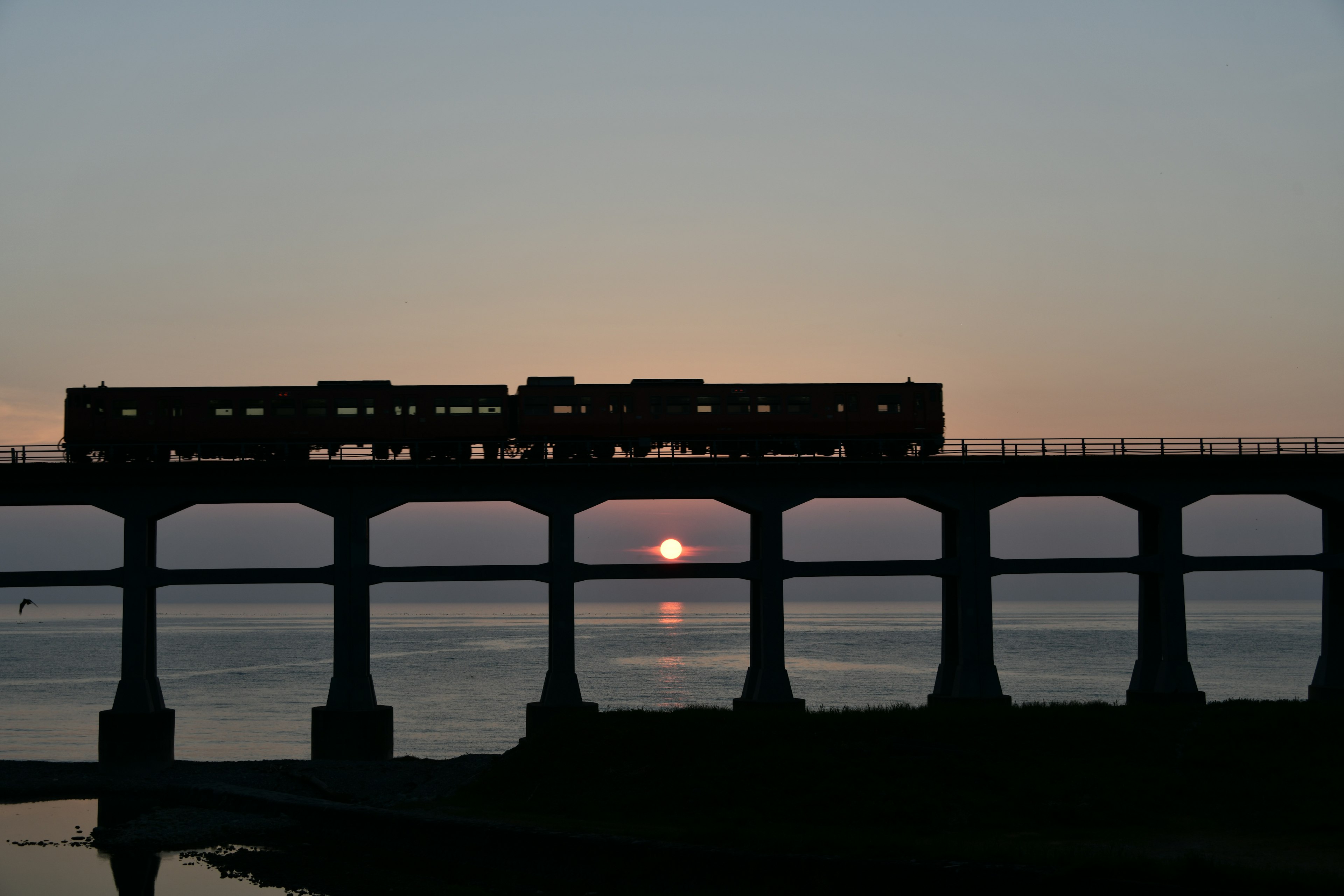 Silhouette eines Zuges, der eine Eisenbahnbrücke bei Sonnenuntergang überquert