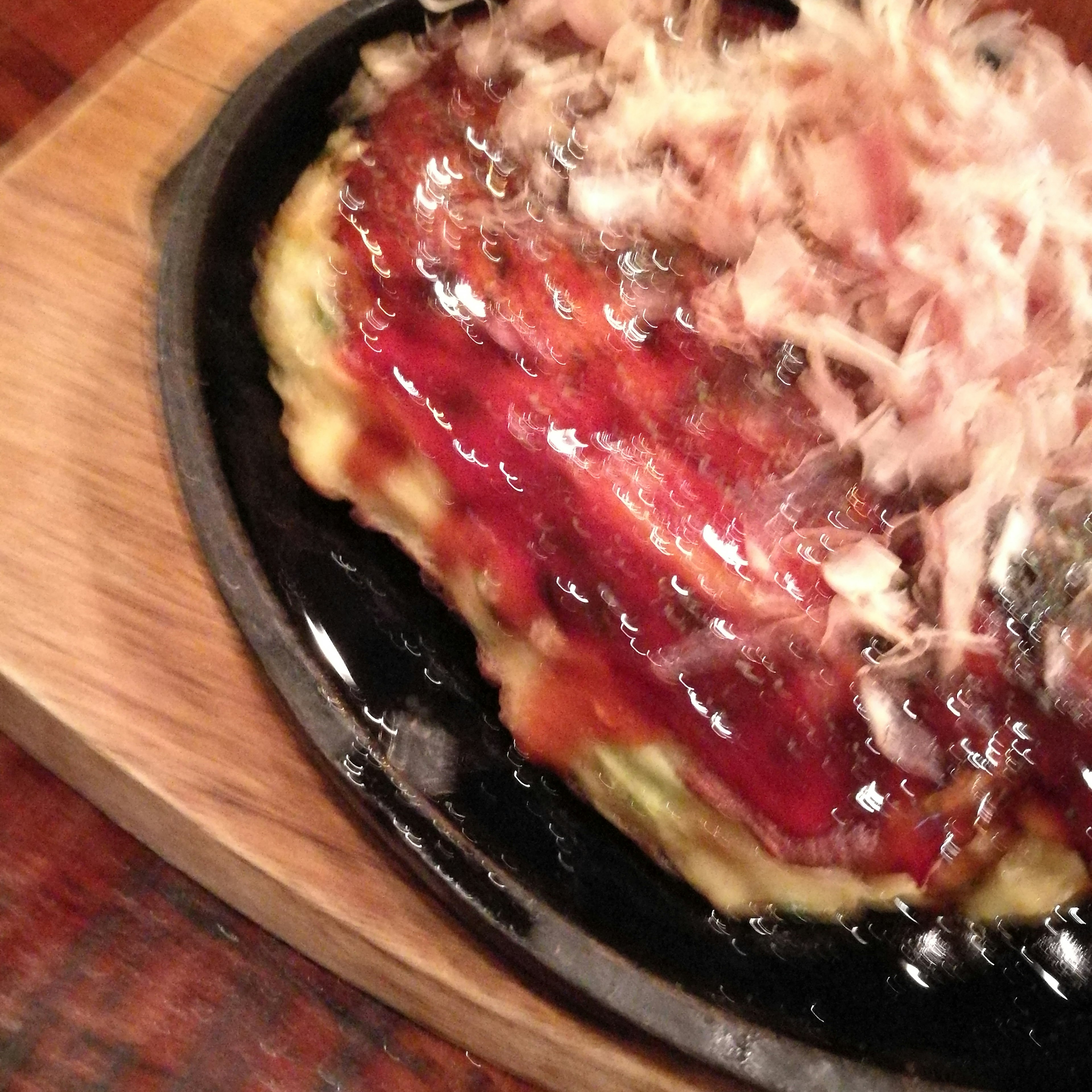 Okonomiyaki served on a sizzling plate topped with sauce and bonito flakes