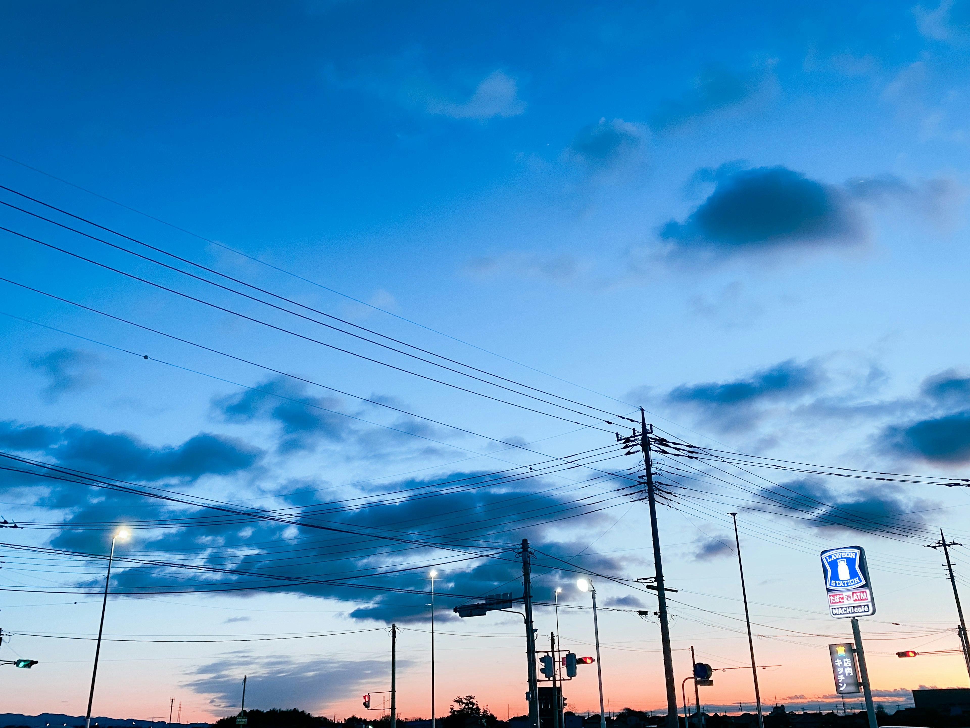 Cielo azul vibrante con atardecer naranja visible Líneas eléctricas y farolas en primer plano