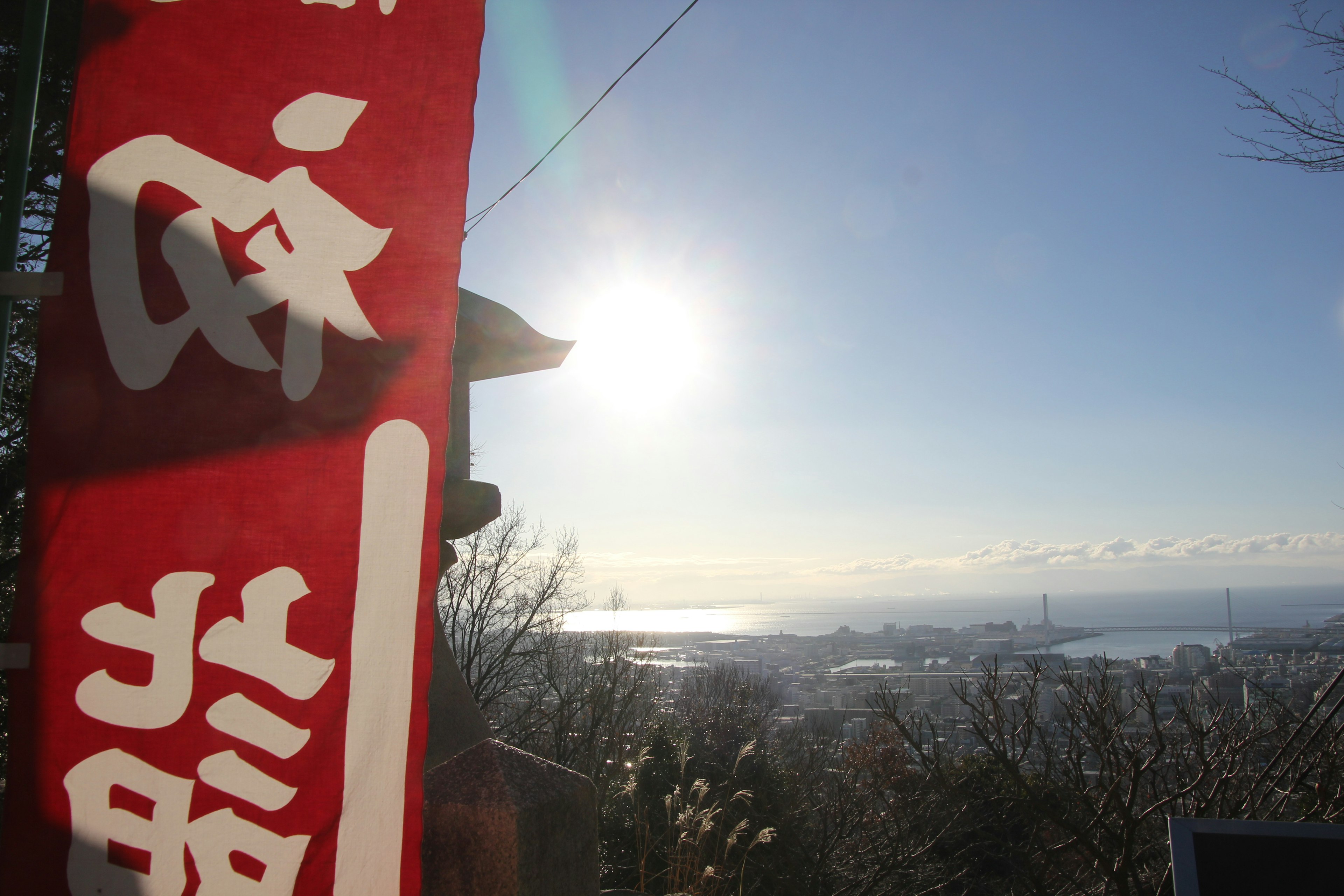 Bandera roja con kanji frente a un amanecer y vista del océano