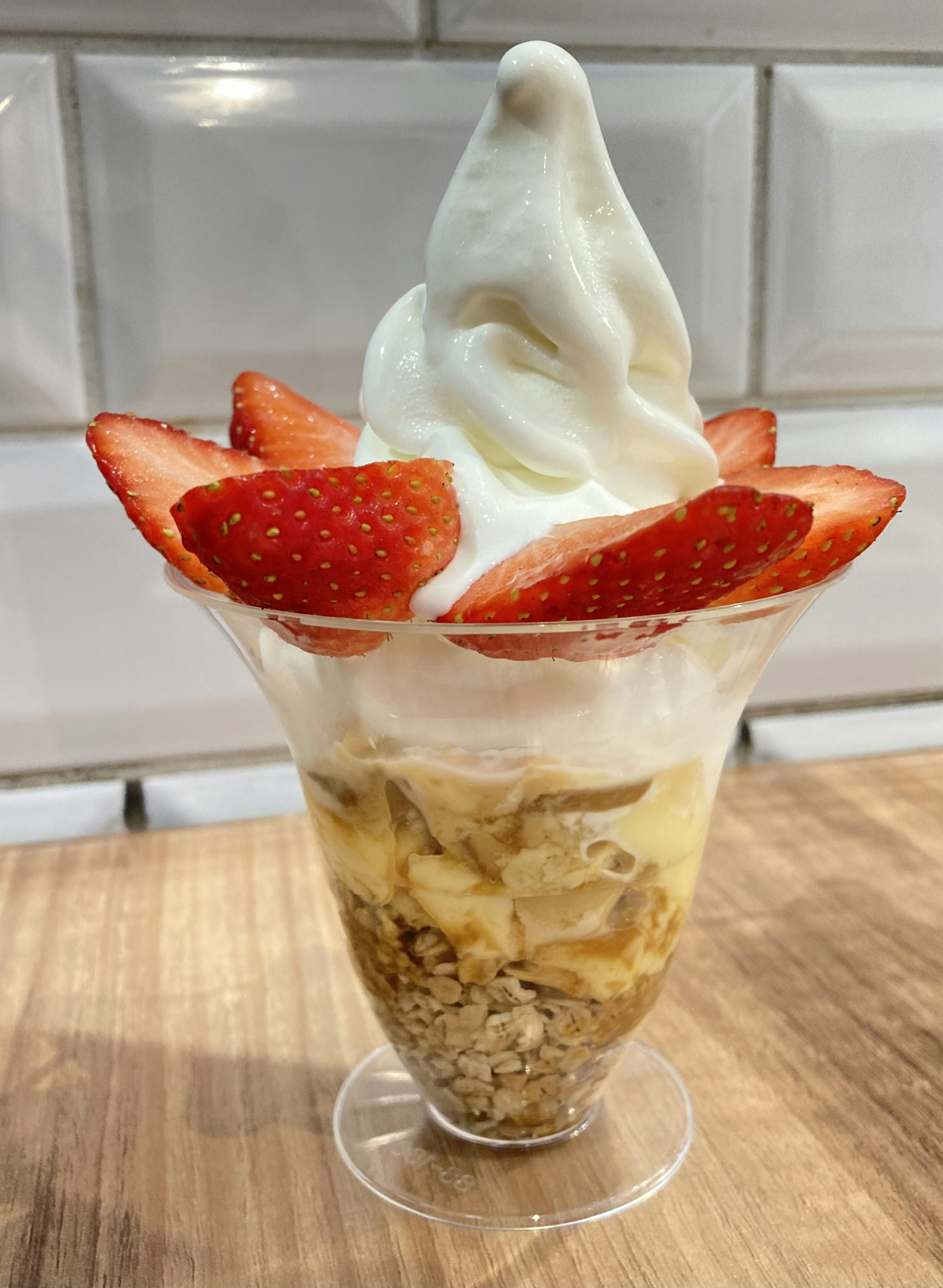 Strawberry parfait topped with soft serve ice cream featuring a layered dessert with granola and banana