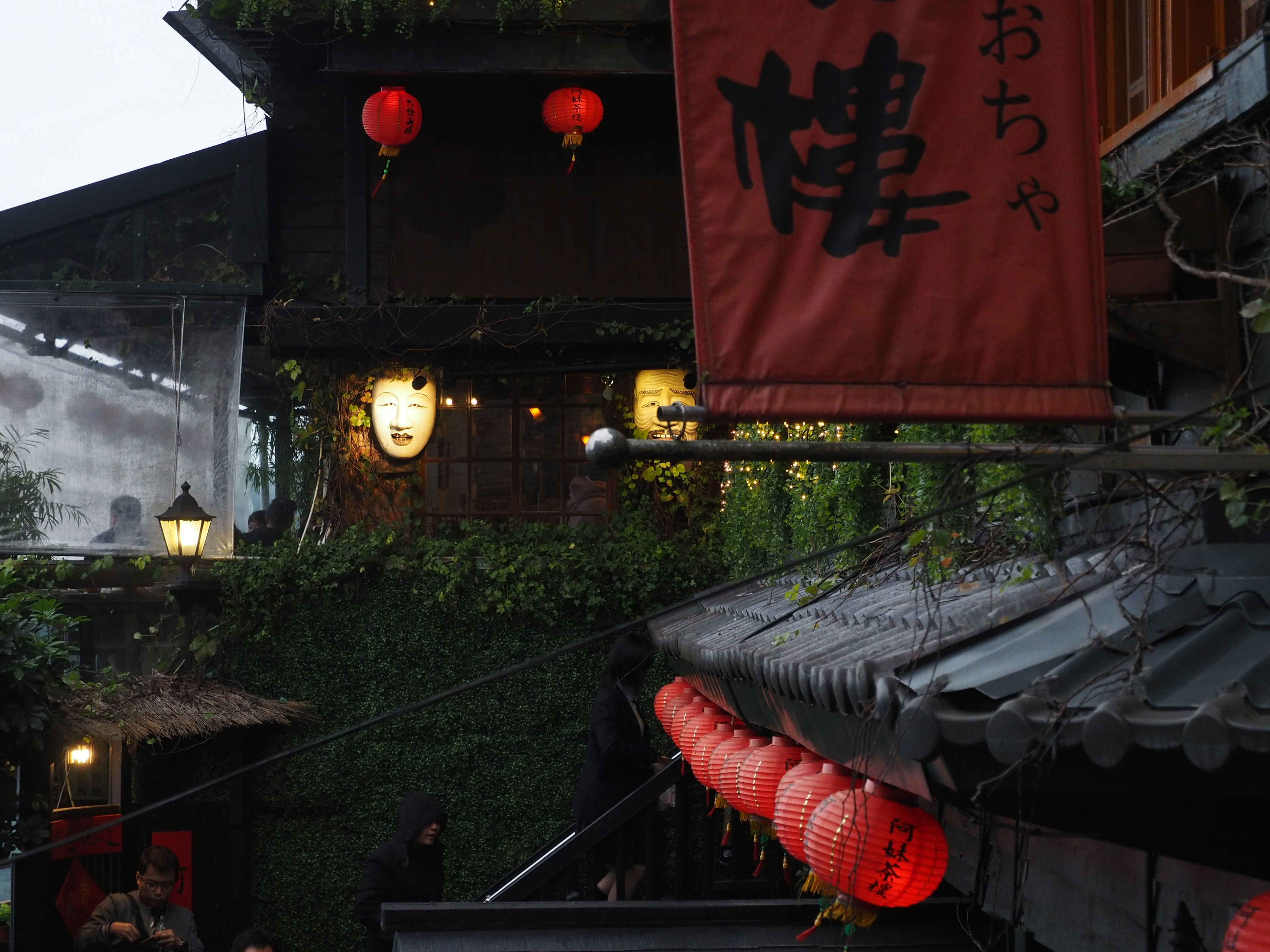 Traditional Japanese street scene in the rain featuring red lanterns and a sign