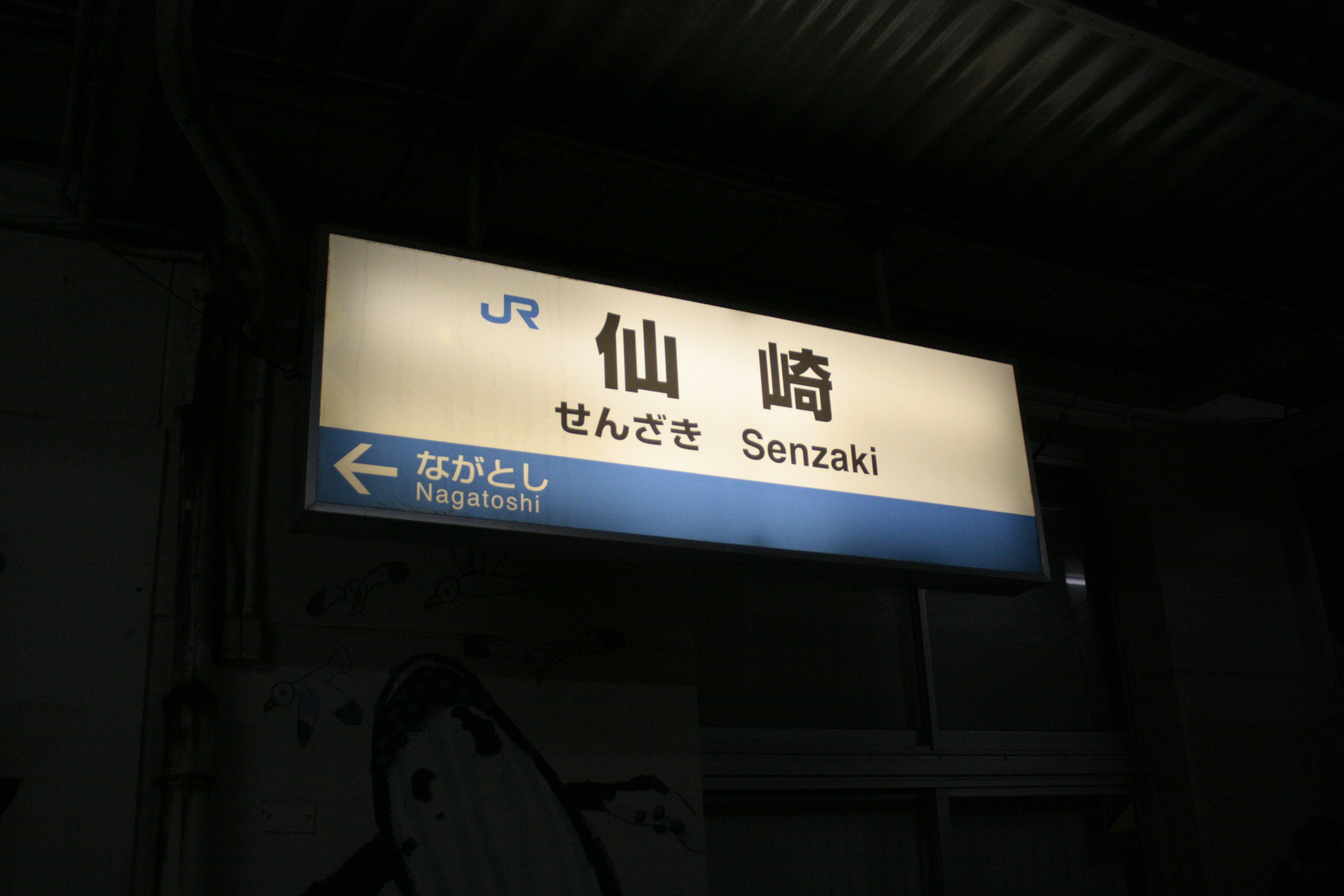 Senzaki Station sign with JR logo illuminated in dark background