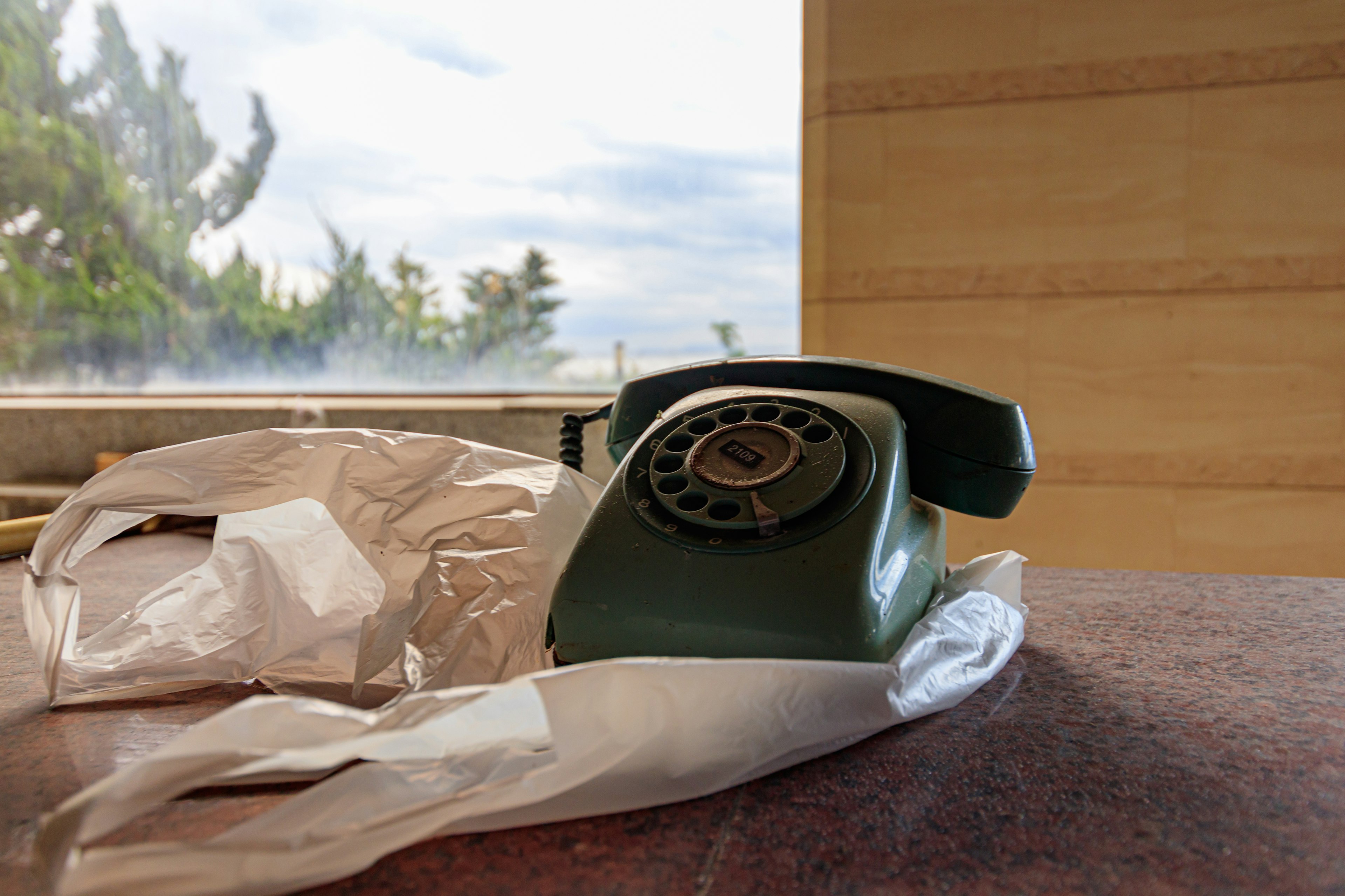 Un teléfono de disco verde colocado cerca de una ventana con vista a los árboles