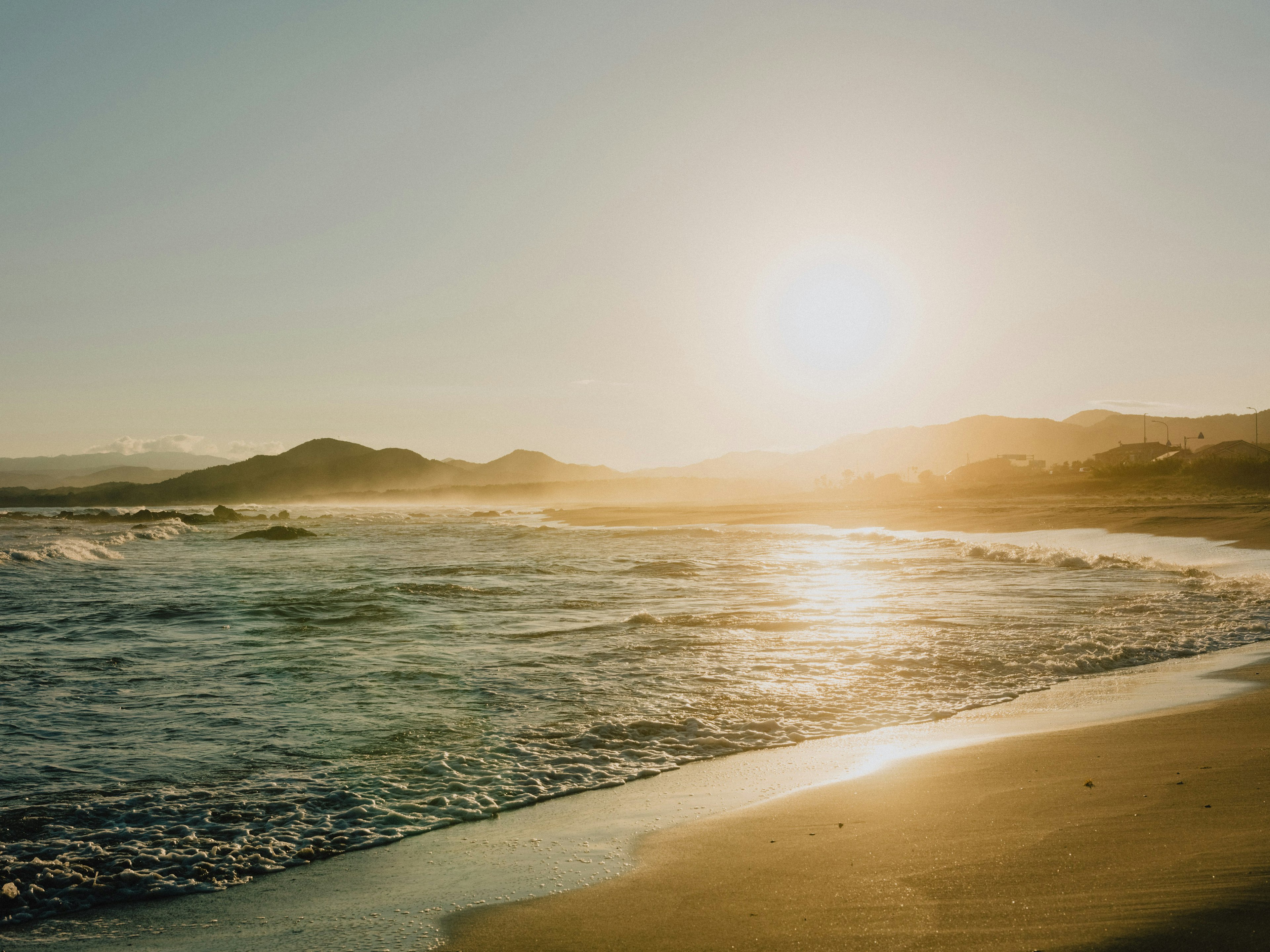 Coucher de soleil sur la plage avec des vagues et des collines au loin