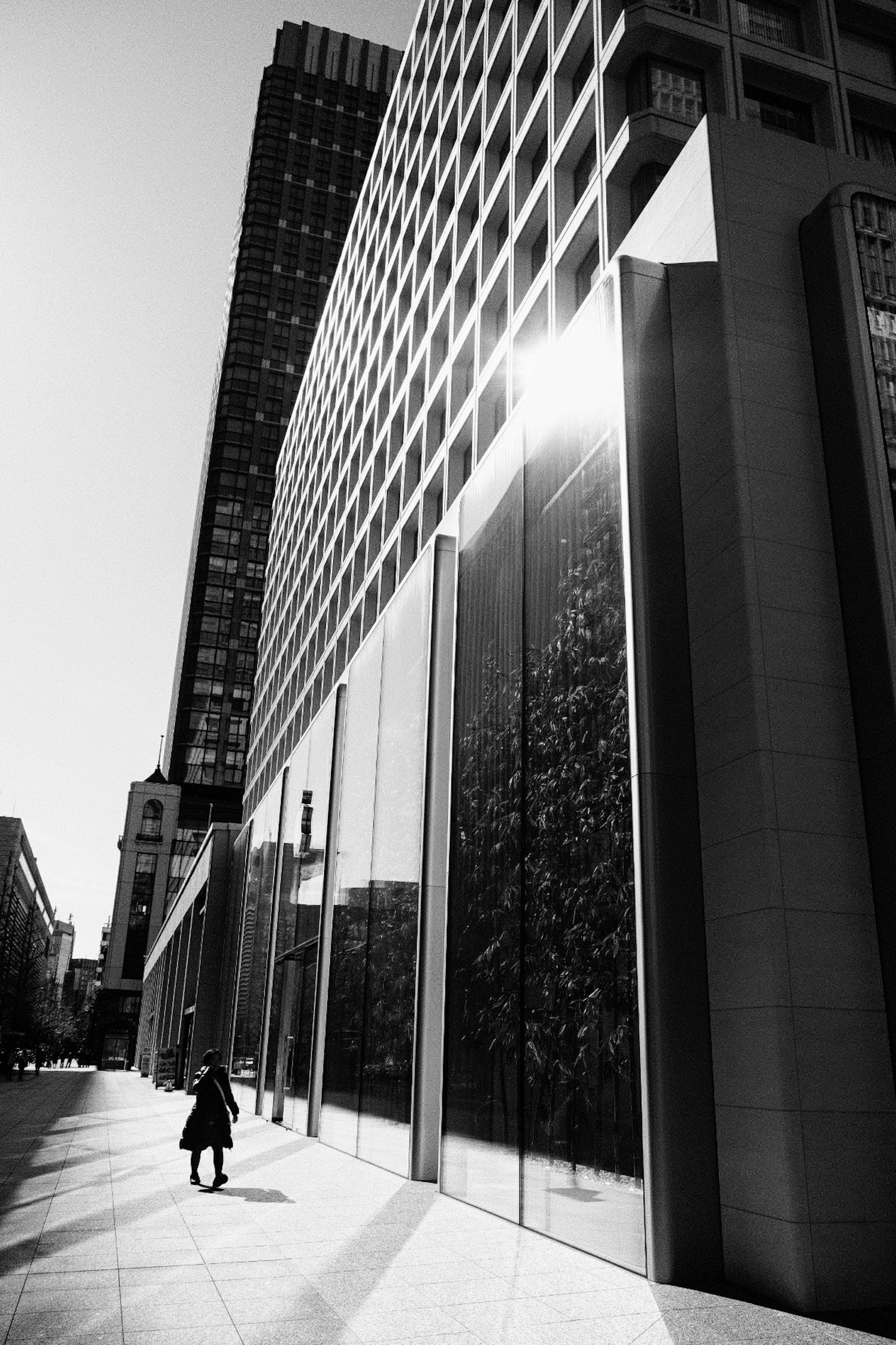 A woman walking in a monochrome urban scene with reflections of skyscrapers