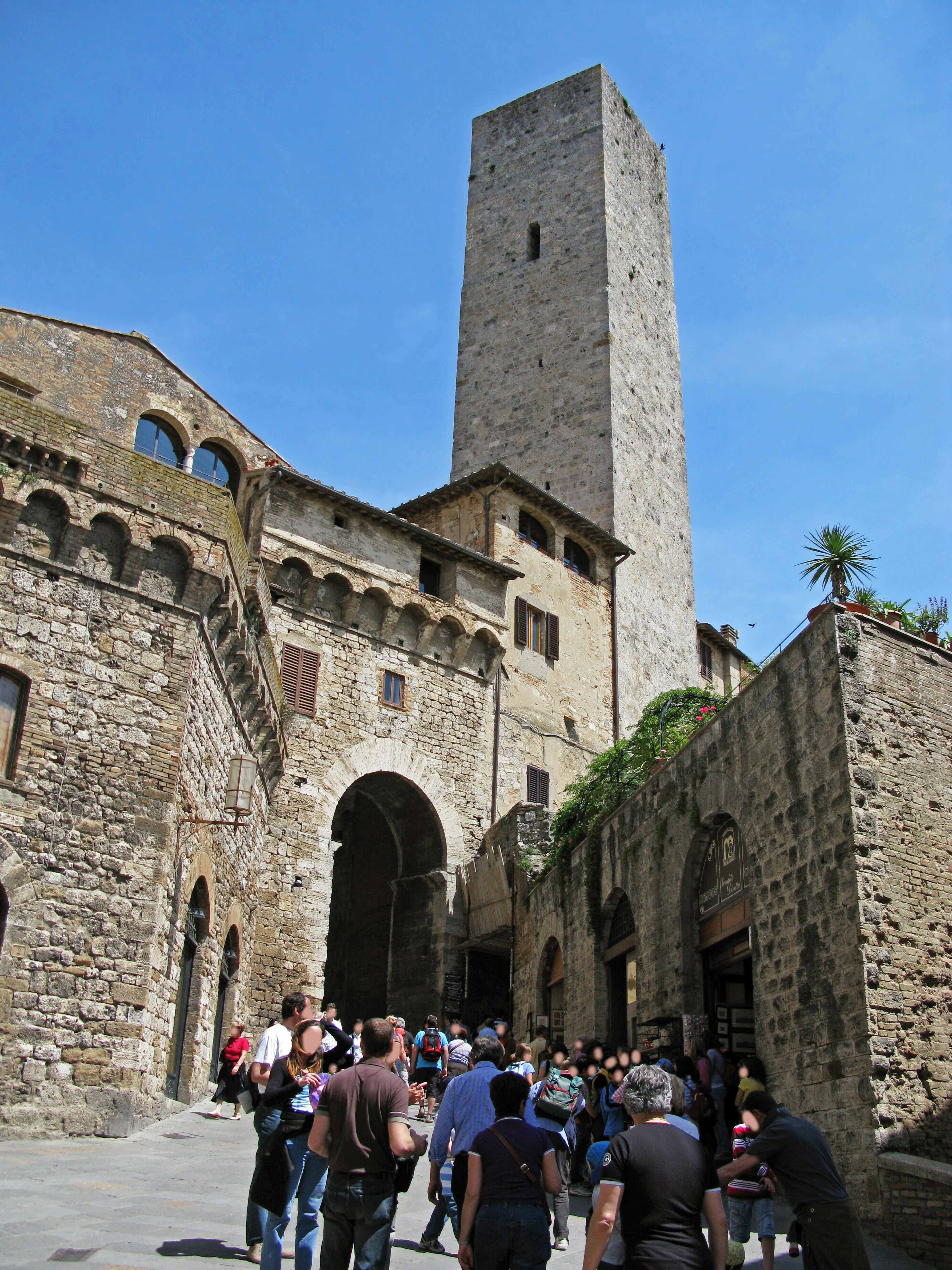 Personas caminando en un pueblo medieval con una alta torre de piedra