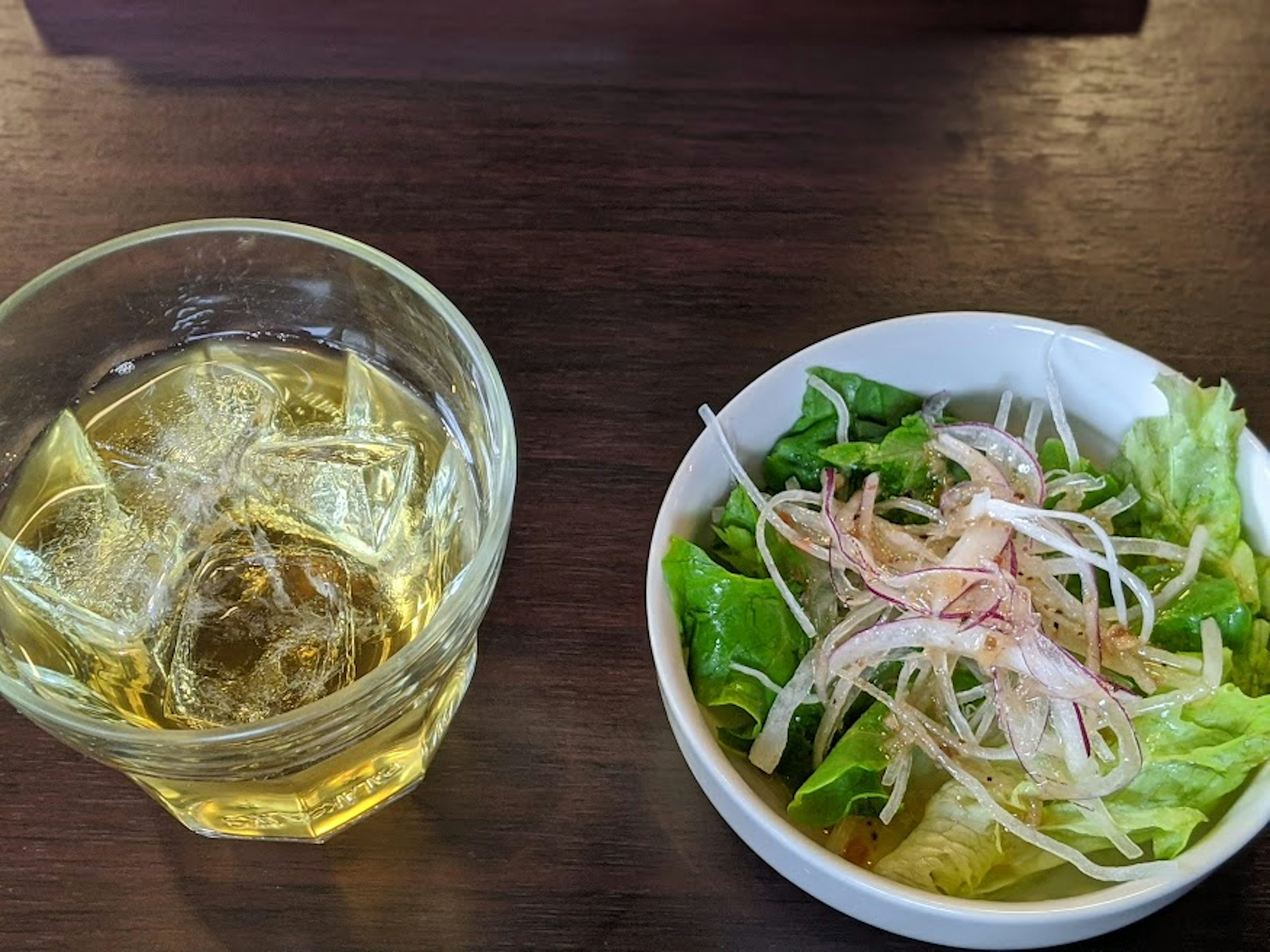 Un vaso de bebida con hielo junto a un tazón de ensalada fresca