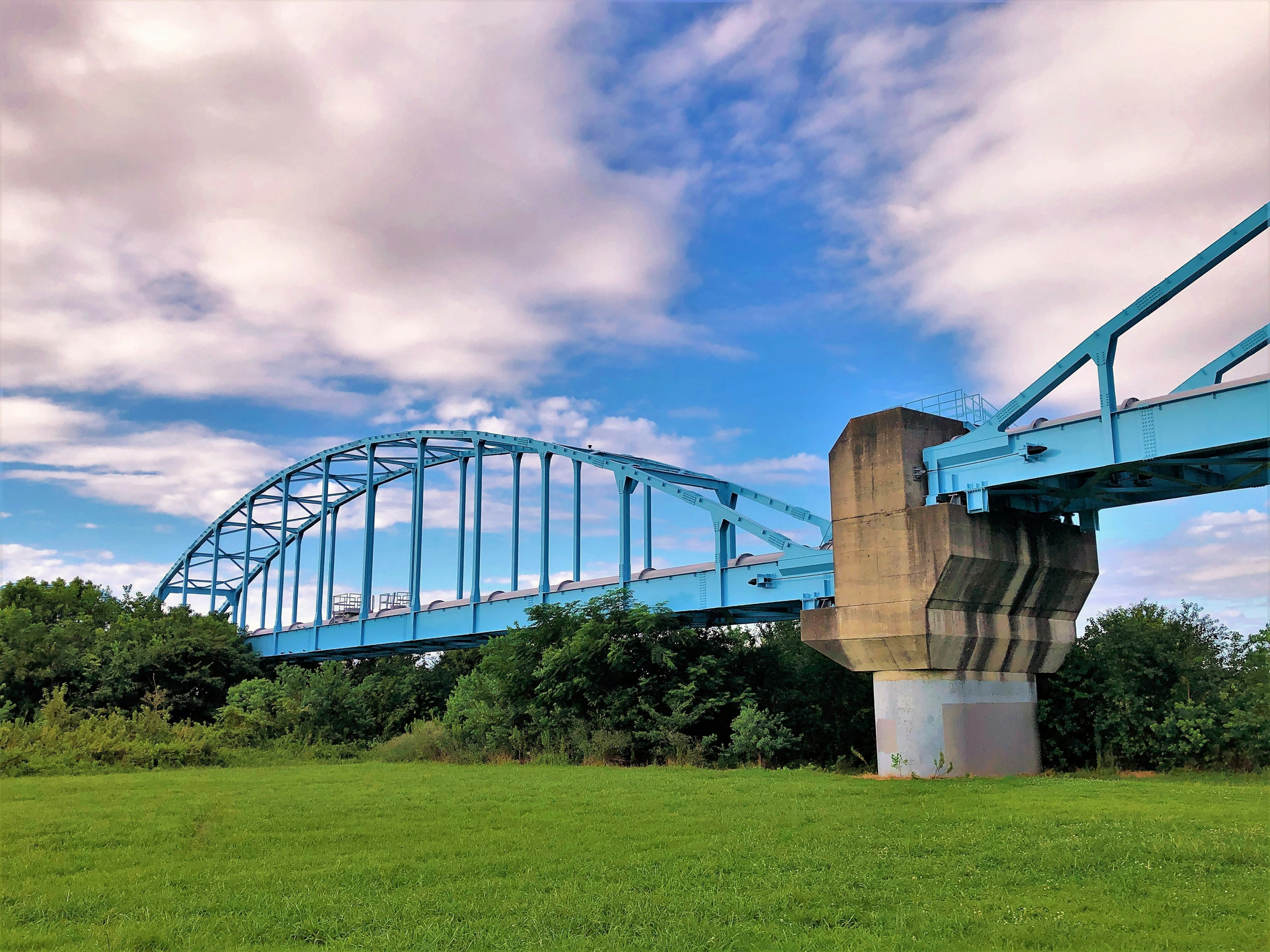 A blue arch bridge under a blue sky with clouds