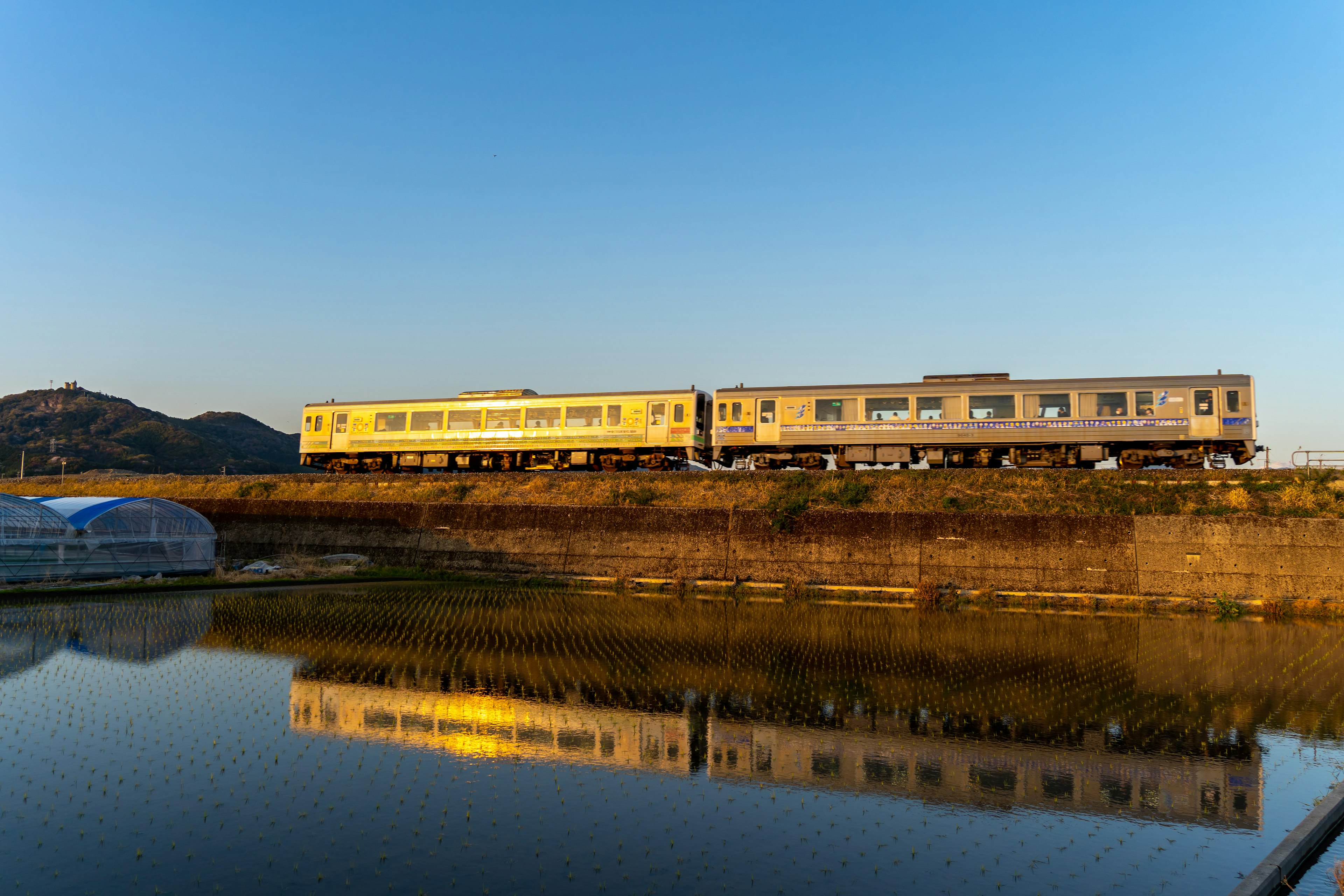 Tren plateado corriendo bajo un cielo de atardecer con su reflejo en el agua