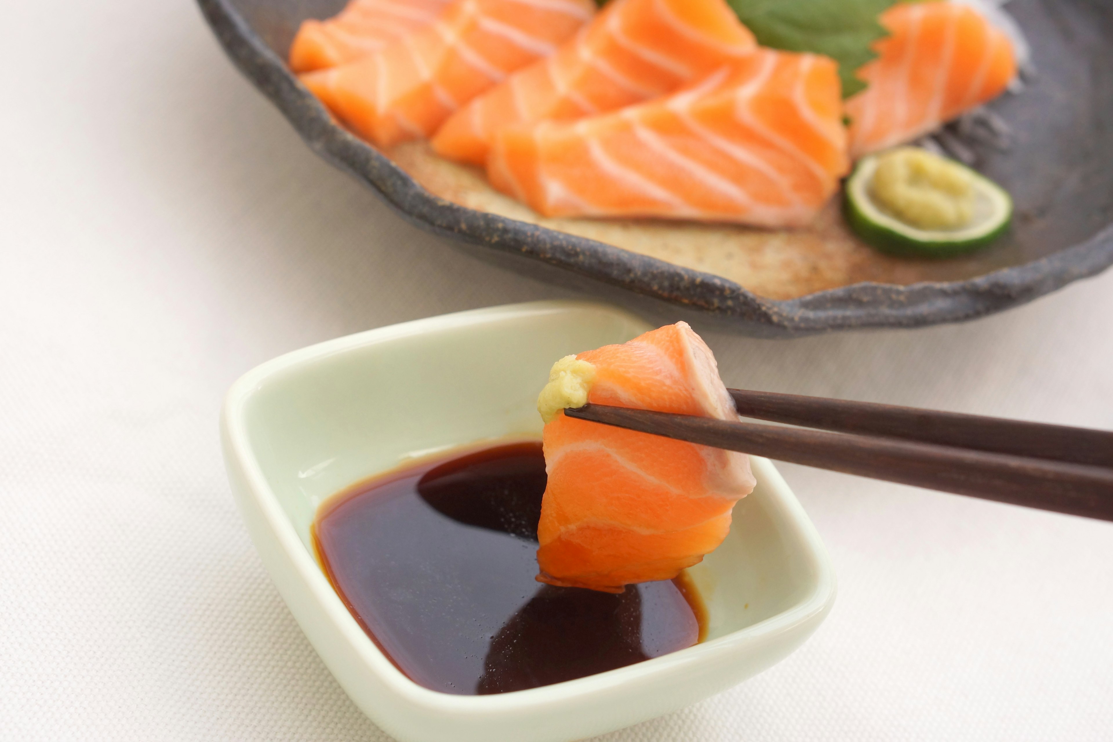 In Scheiben geschnittenes Lachs-Sashimi mit einer kleinen Schüssel Sojasauce und Essstäbchen