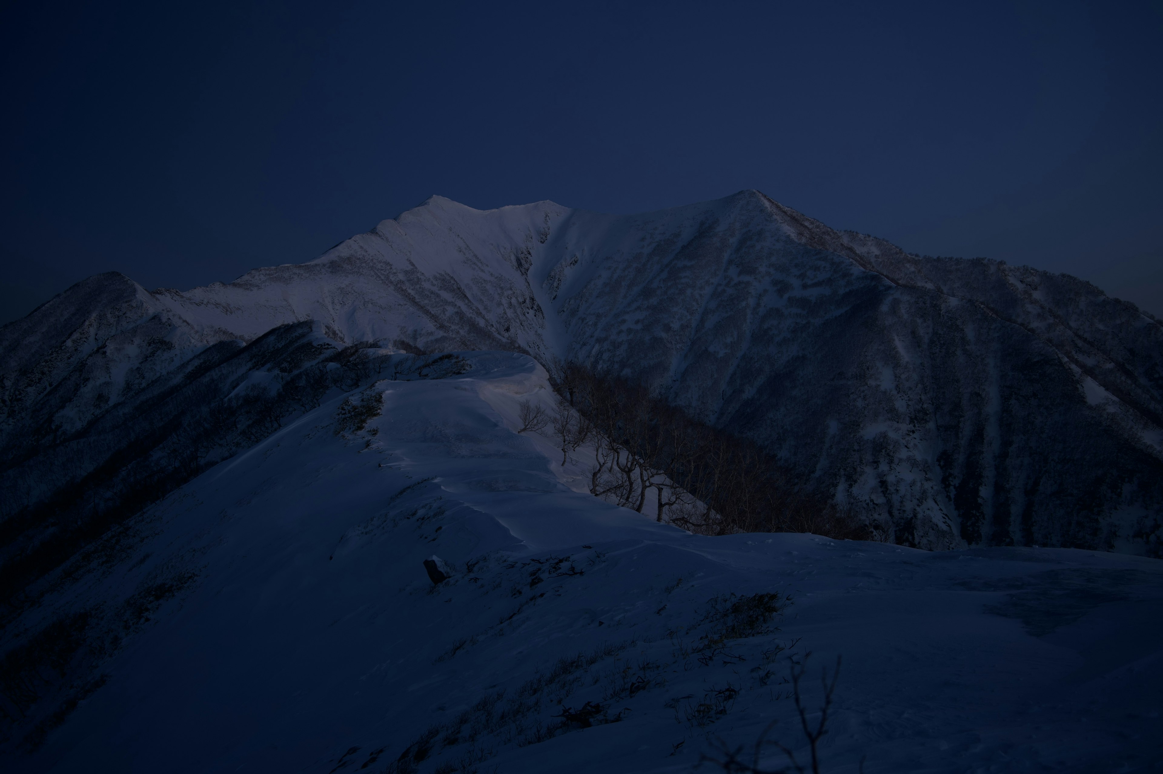 Silhouette de montagnes couvertes de neige sous un ciel bleu foncé