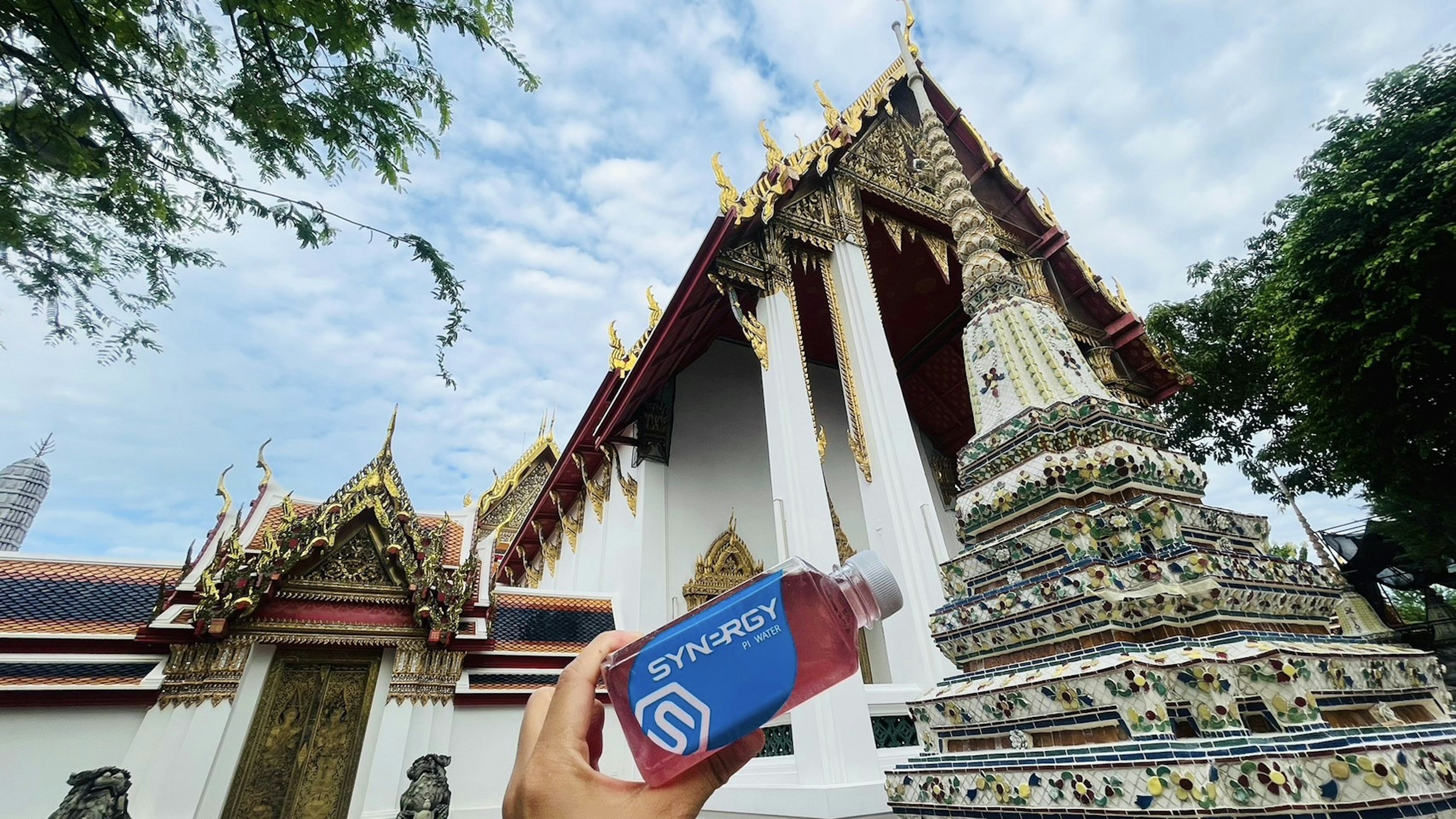 Image of a hand holding a beverage in front of a temple featuring beautiful architecture and a blue sky