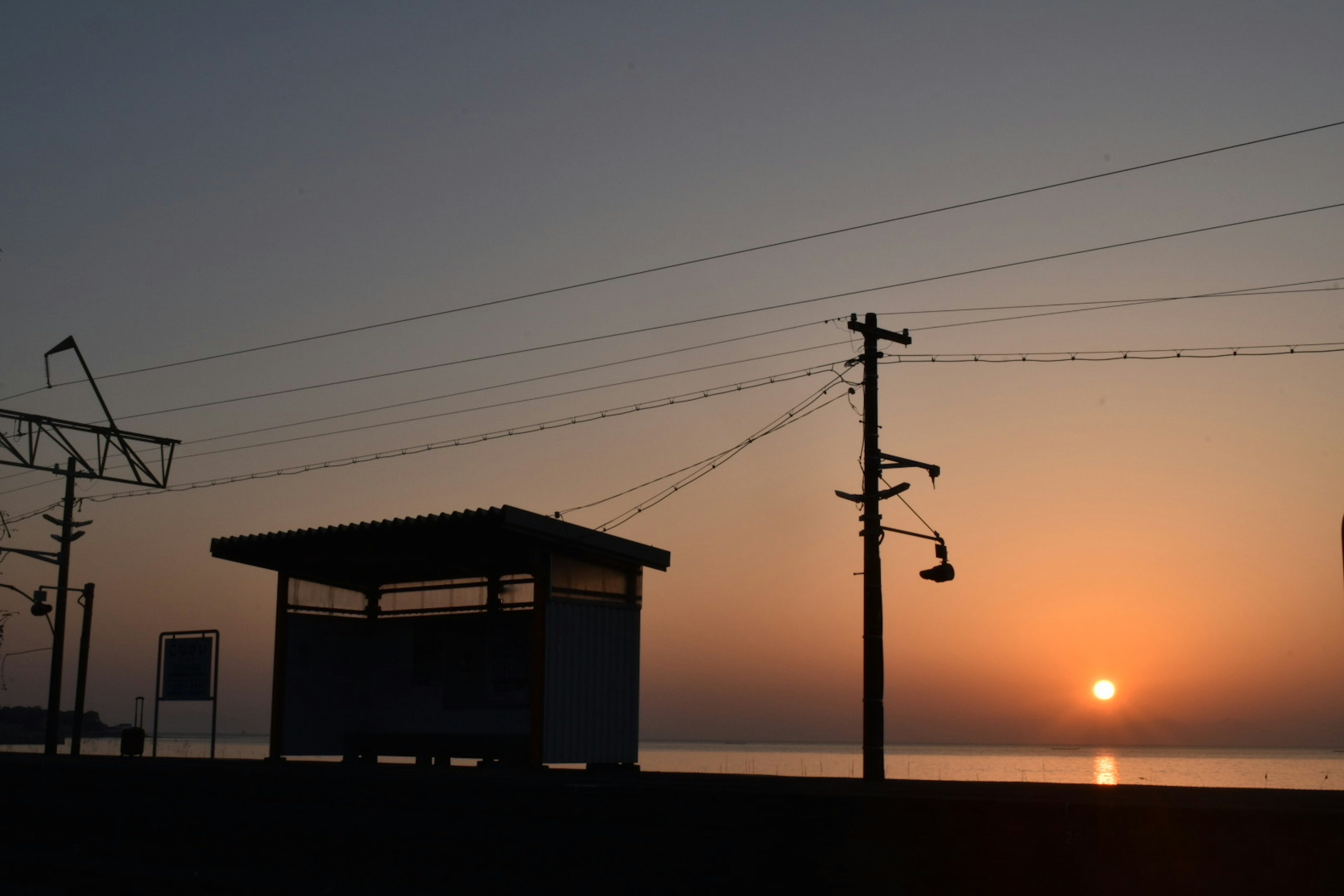 Silhouette einer Bushaltestelle gegen einen Sonnenuntergang über dem Wasser