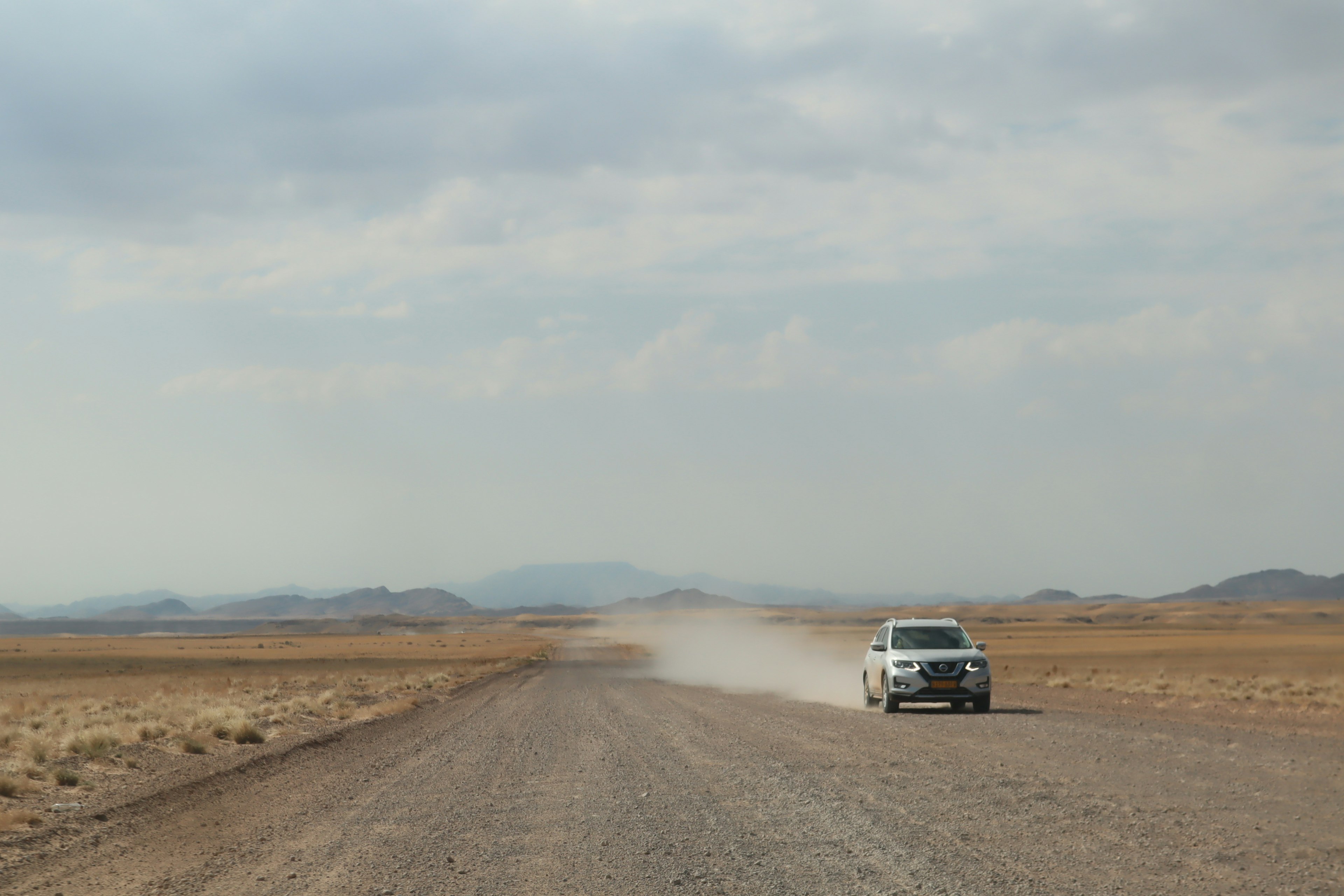 Weißes SUV fährt auf einer staubigen Straße in einer kargen Landschaft