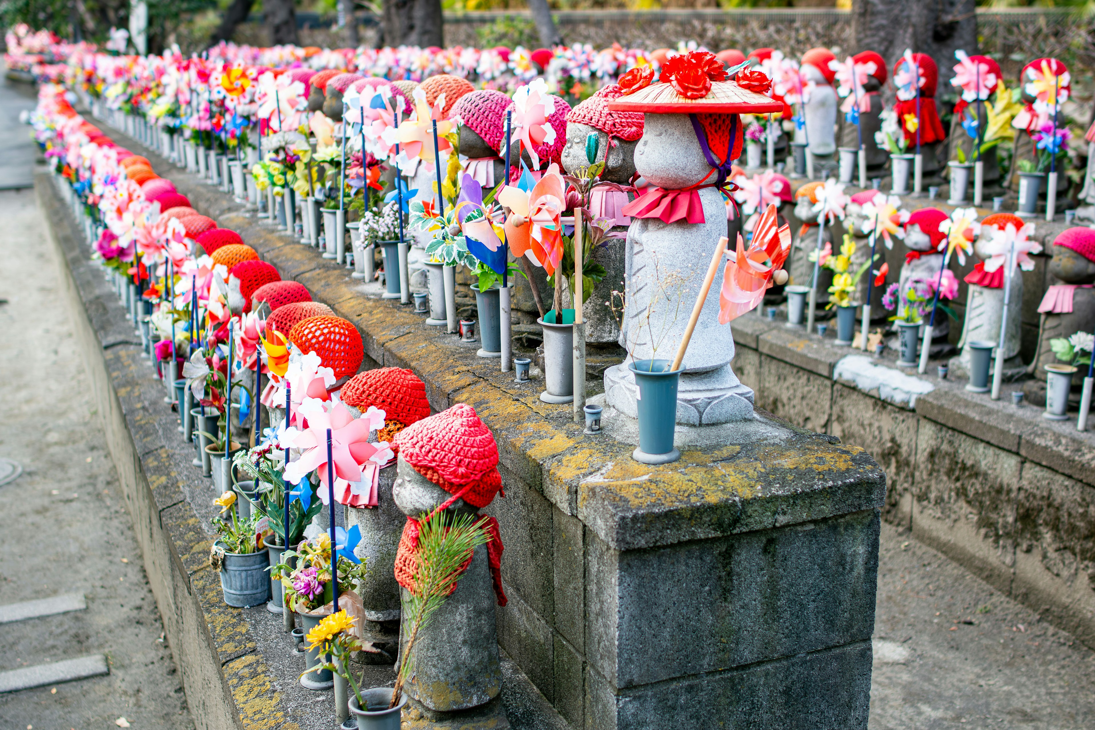 Tượng Jizo đầy màu sắc trang trí bằng hoa và mũ xếp hàng trong một khung cảnh yên bình