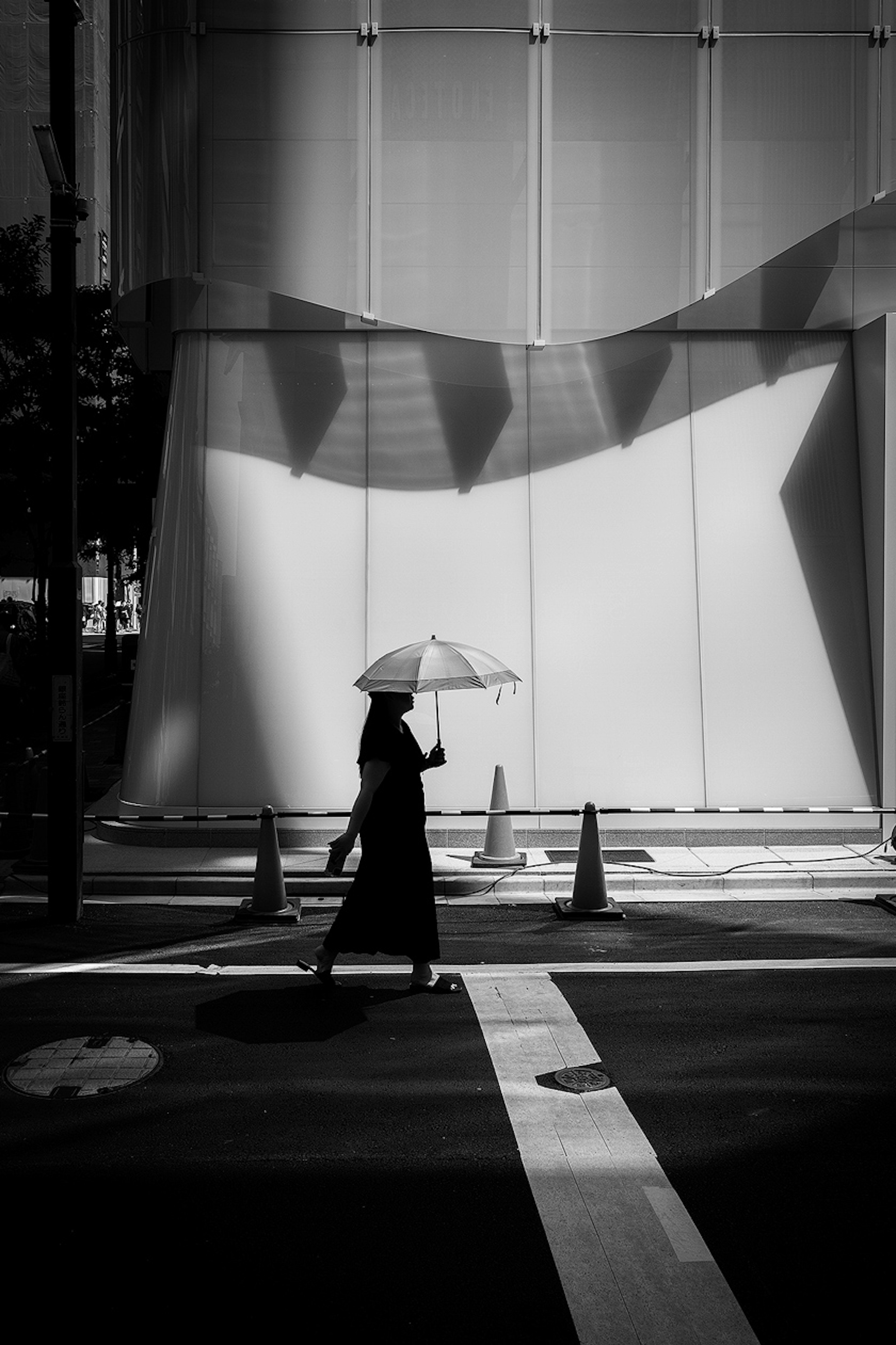 A woman walking with an umbrella at a crosswalk in black and white