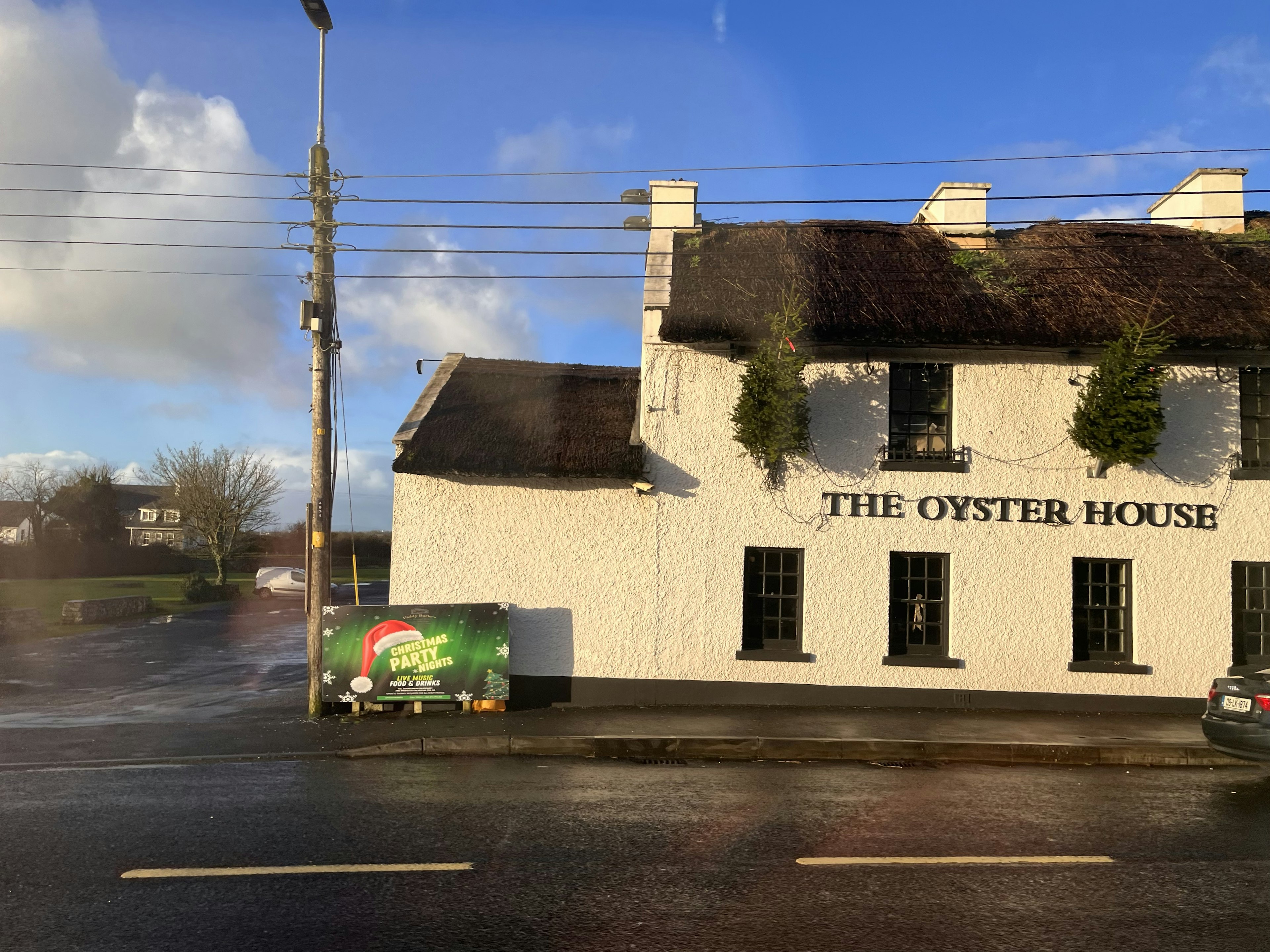 Außenansicht von The Oyster House mit weißen Wänden Strohdach und blauem Himmel