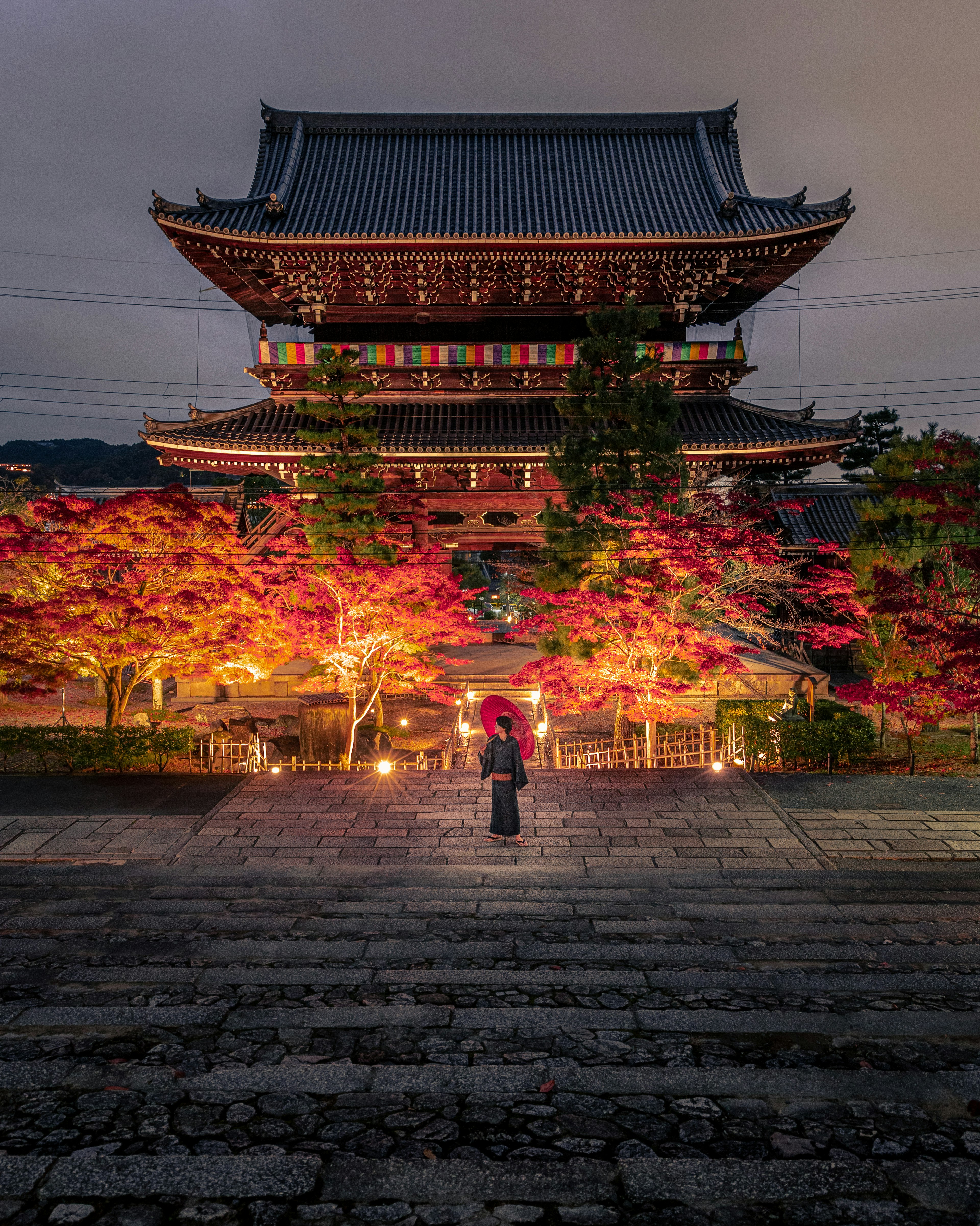 Silhouette einer Person vor einem traditionellen japanischen Tempel umgeben von lebhaften Herbstblättern