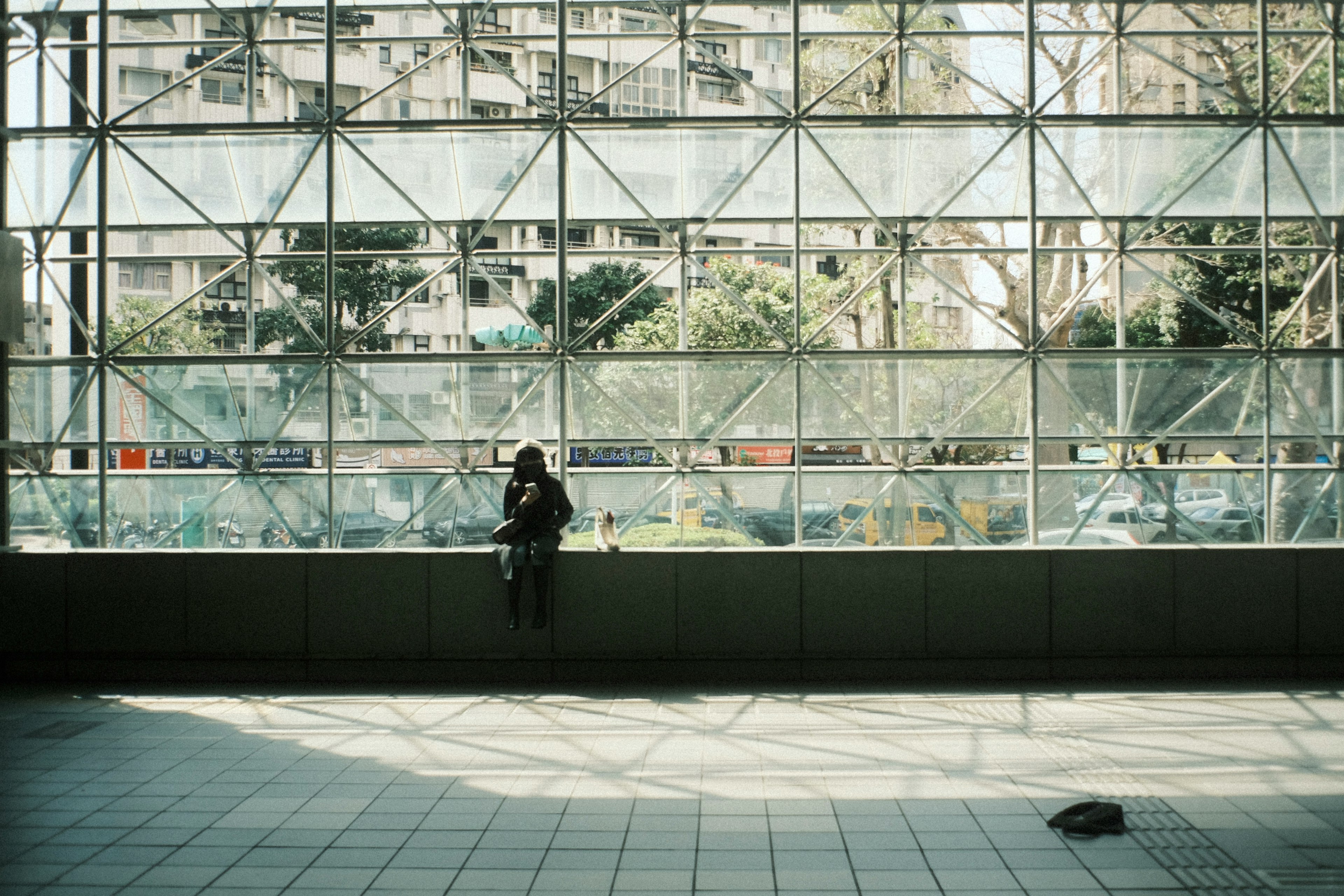 Woman sitting against a wall in a modern building with large windows