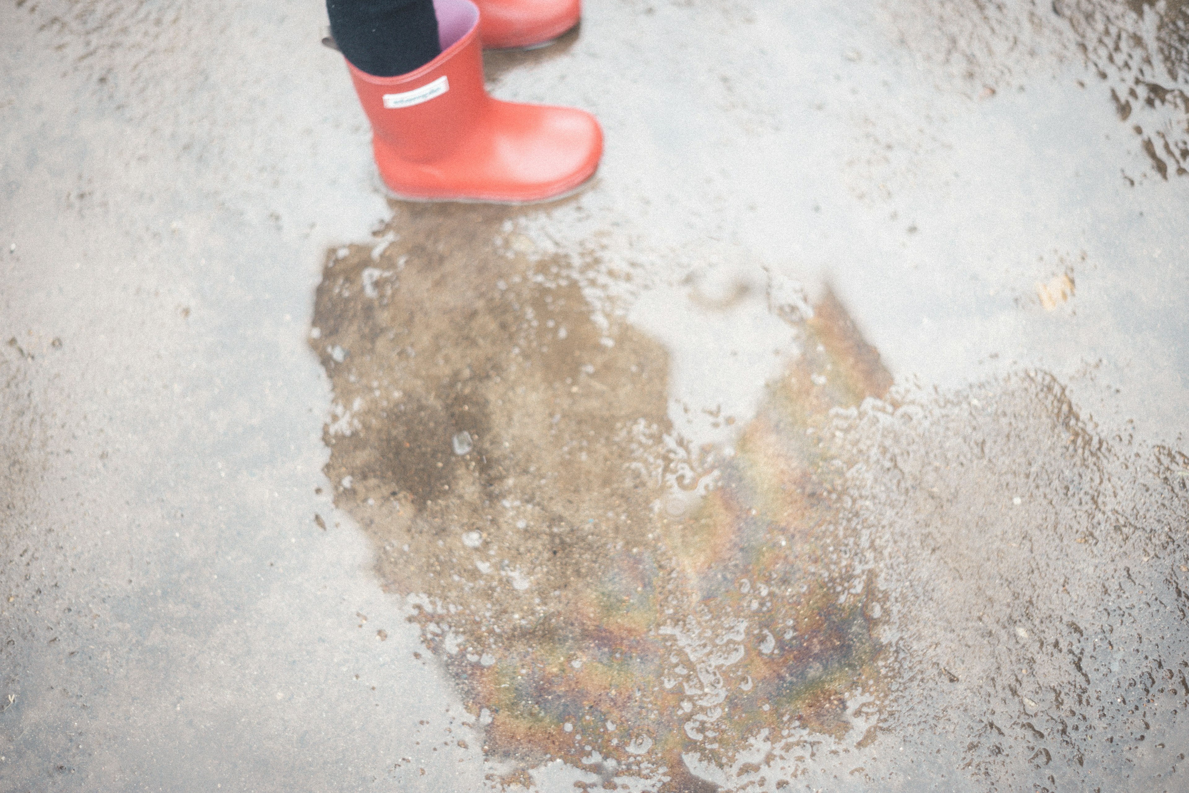 Foot in red rubber boots standing next to a puddle on a textured surface