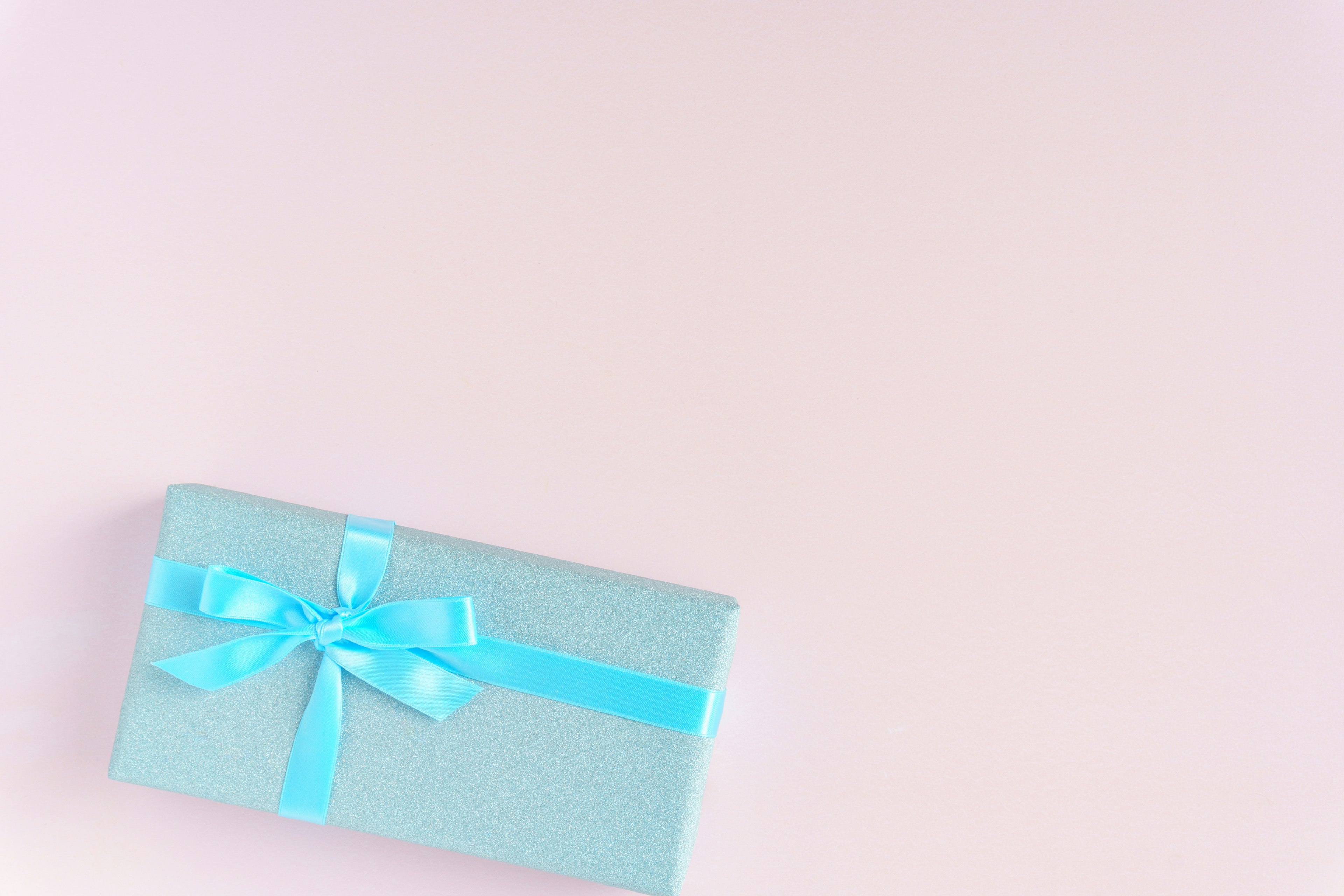 A light blue gift box with a blue ribbon on a soft pink background