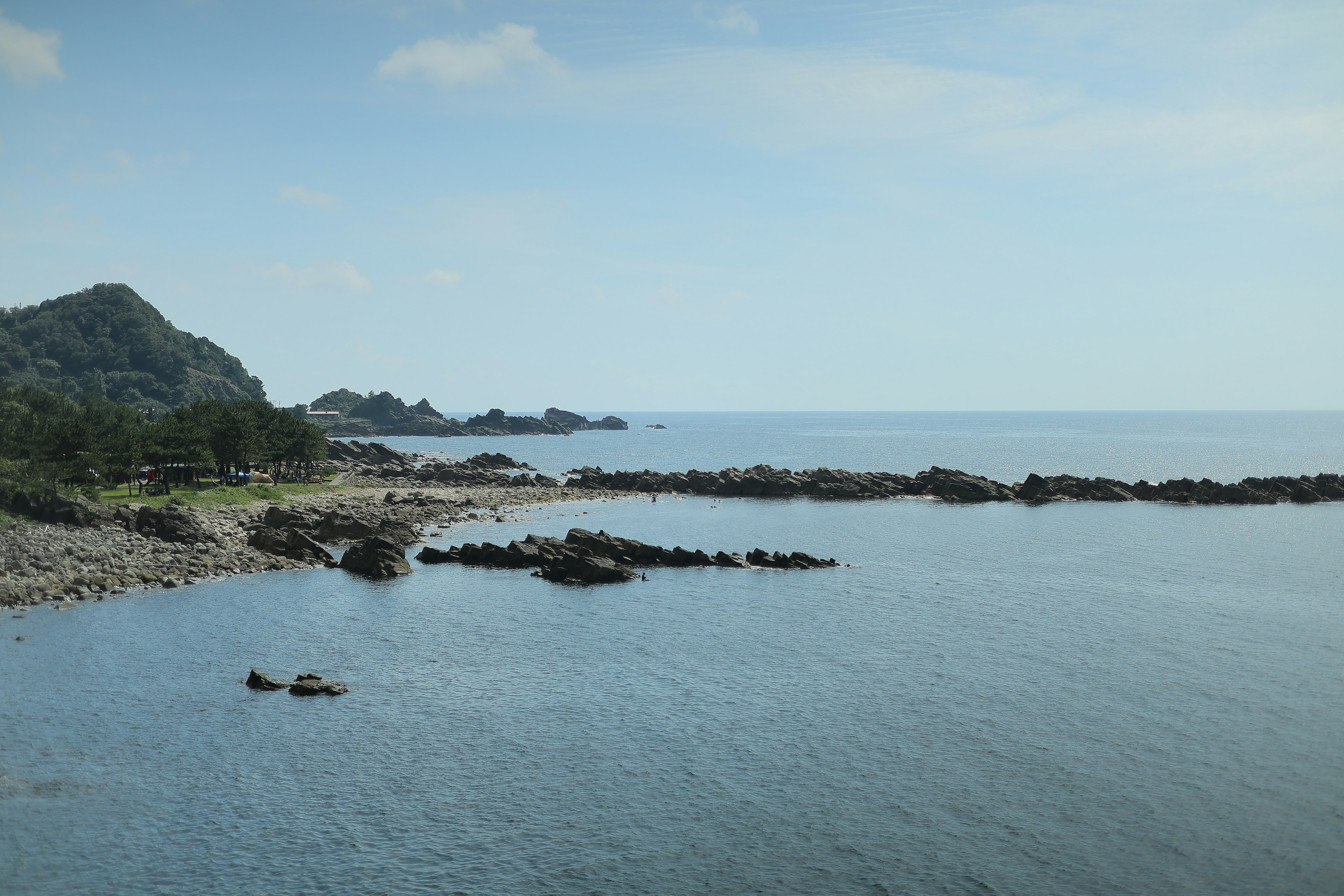 Calm sea with rocky shoreline and distant hills