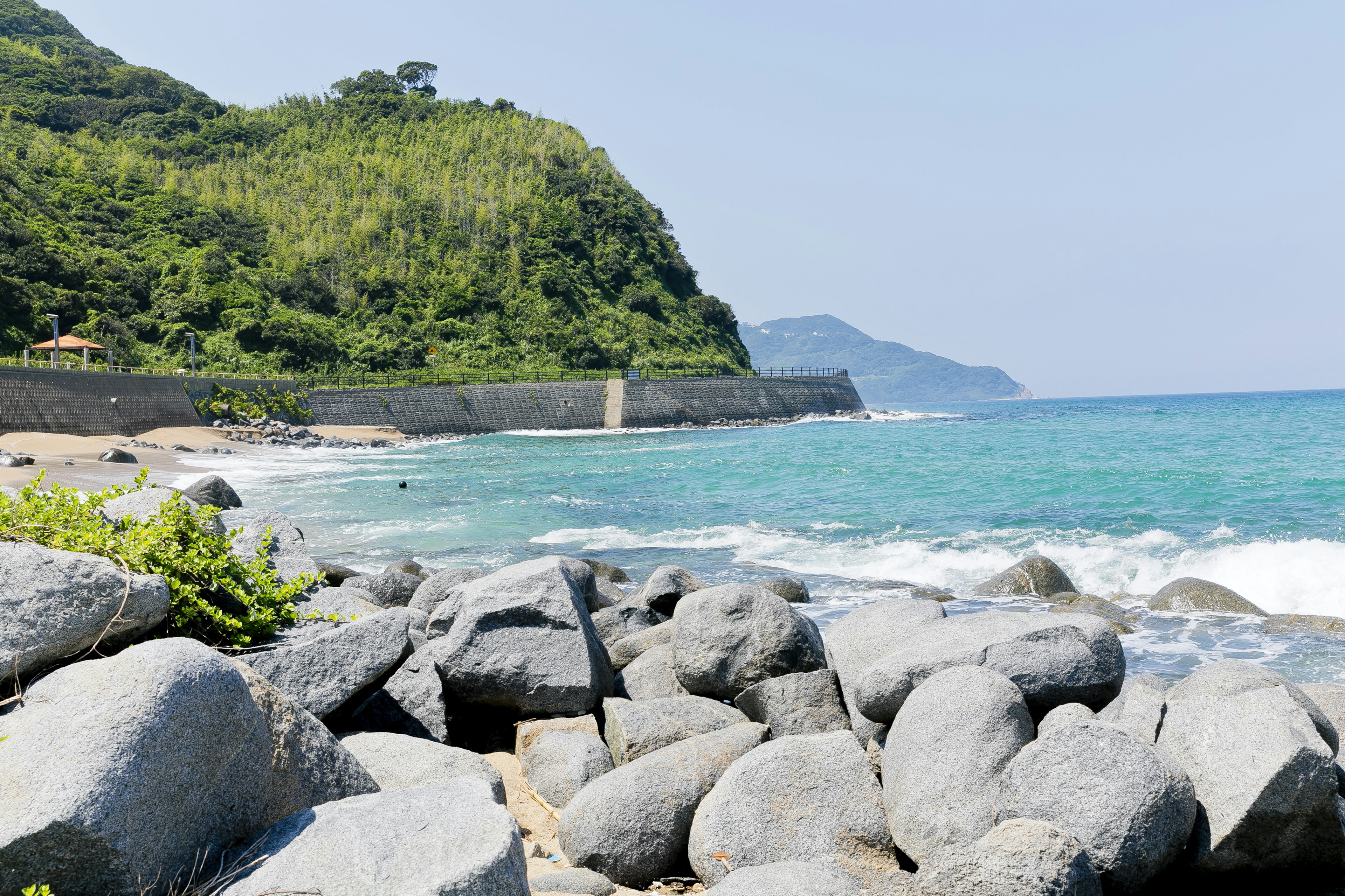 Malersicher Strandblick mit blauem Meer und Felsen grüne Hügel im Hintergrund