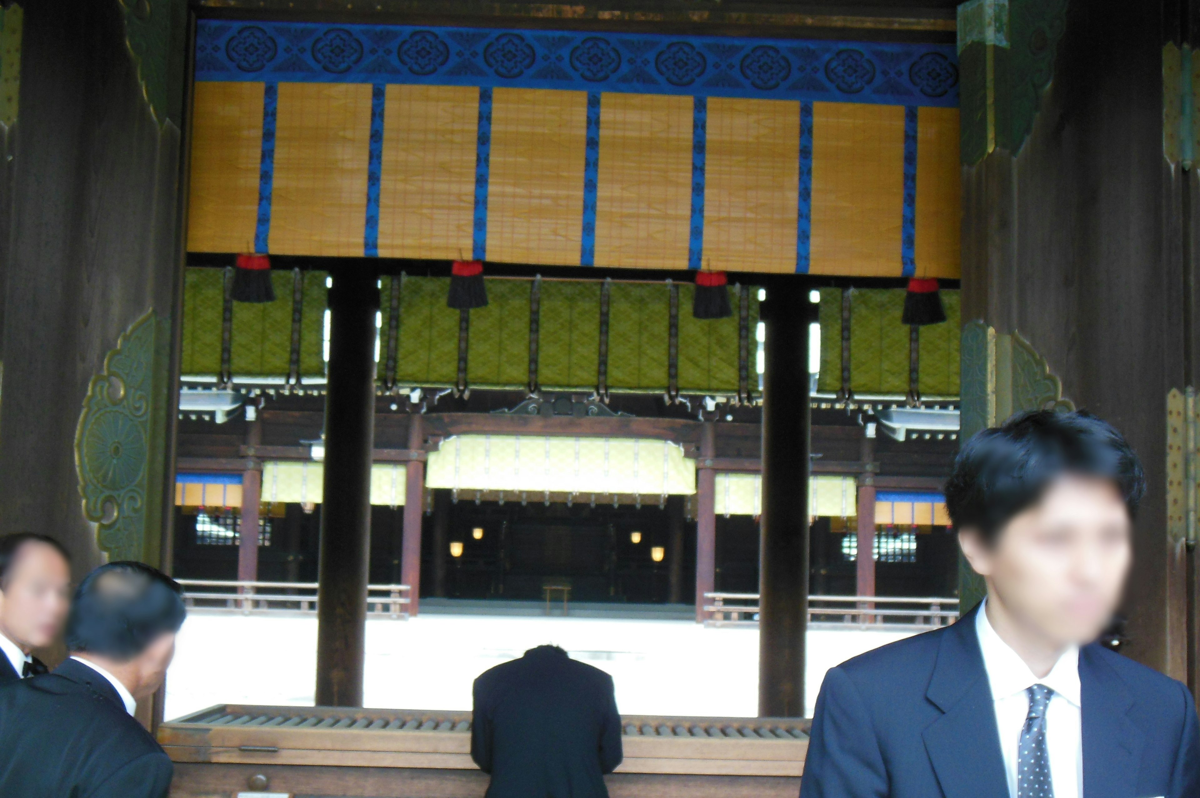 A person bowing inside a quiet shrine with security personnel nearby