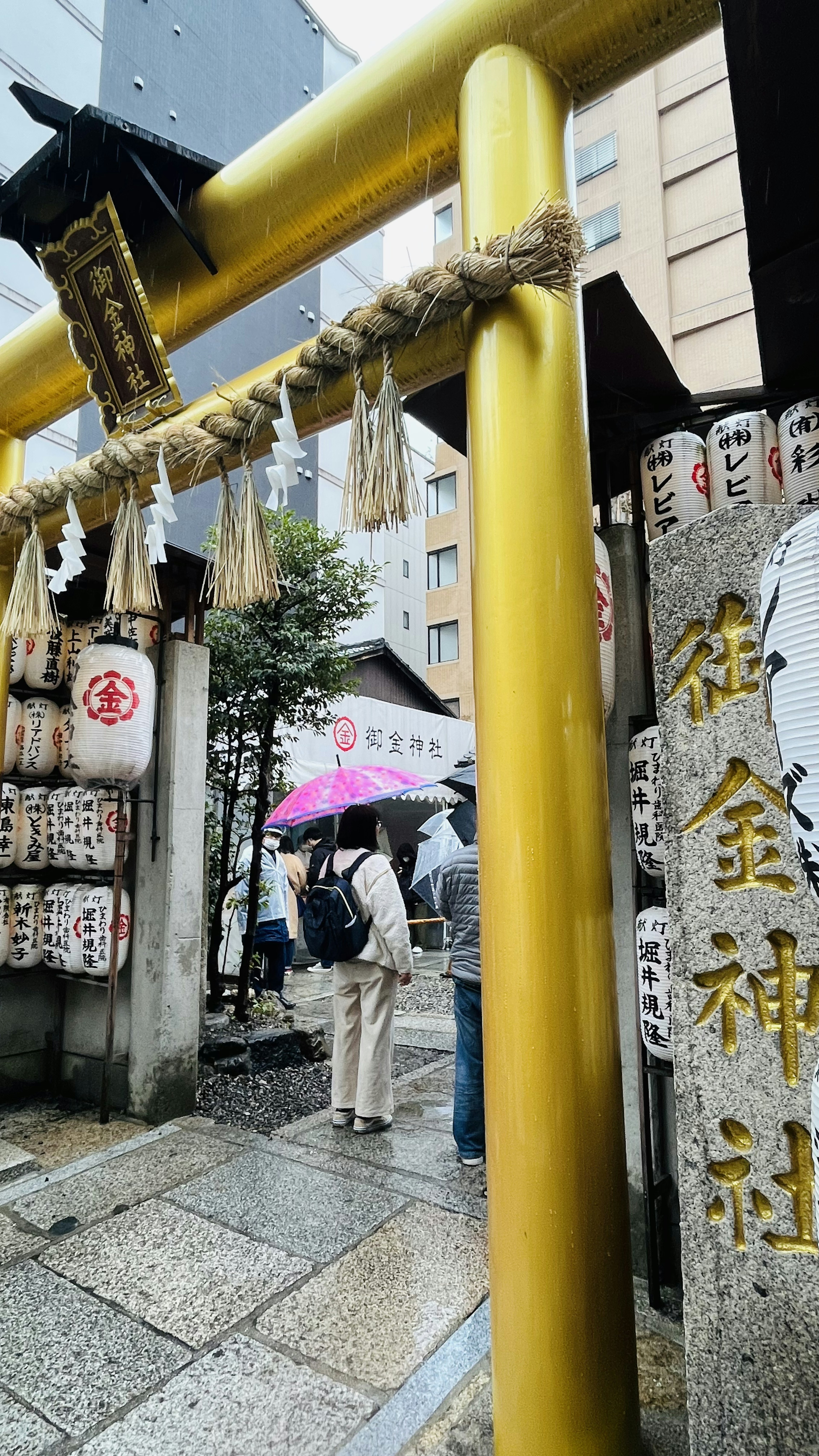 Gerbang torii kuning di pintu masuk kuil dengan wisatawan yang memegang payung di hari hujan