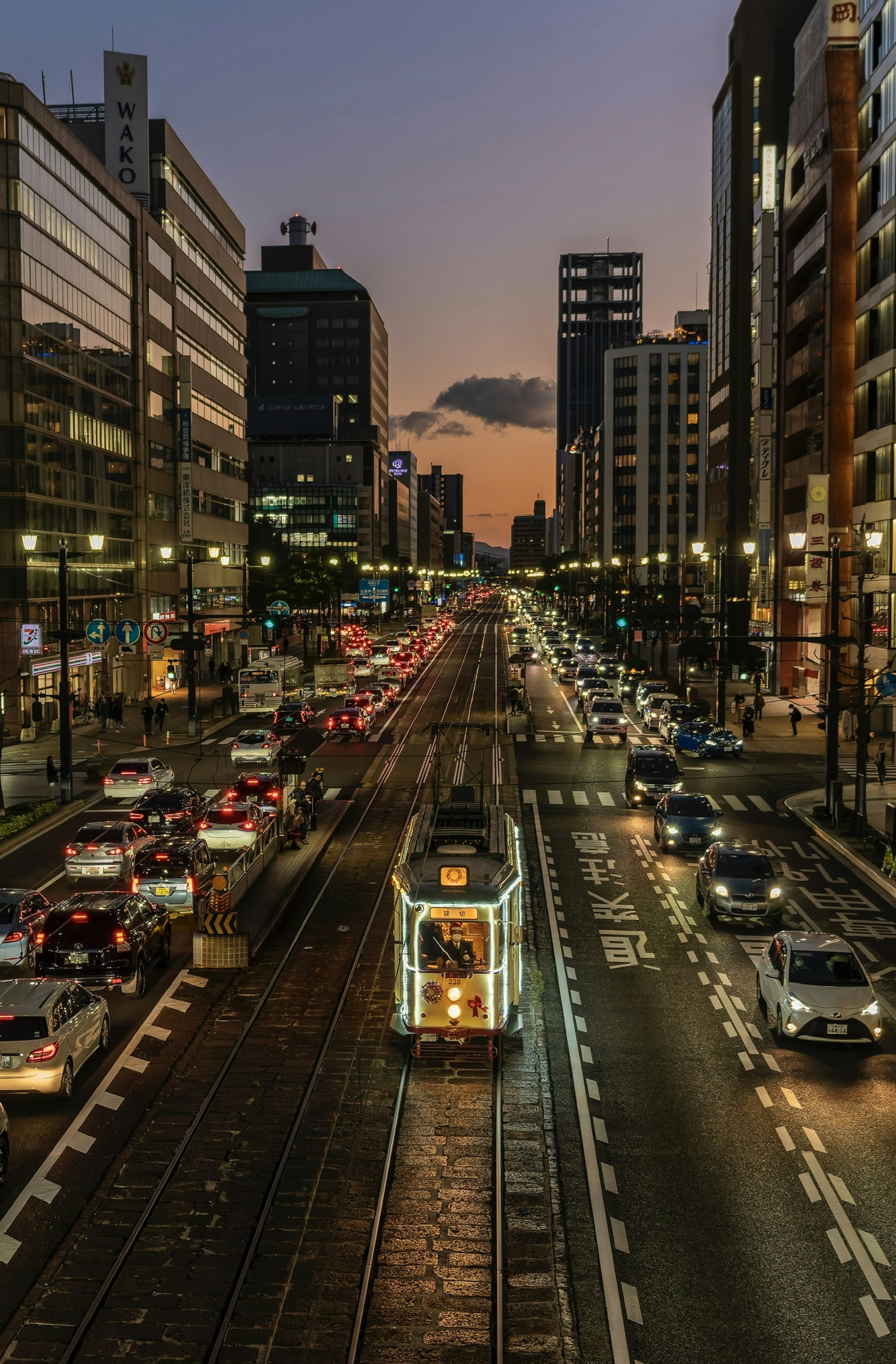 Tram en una calle de la ciudad al anochecer con tráfico concurrido