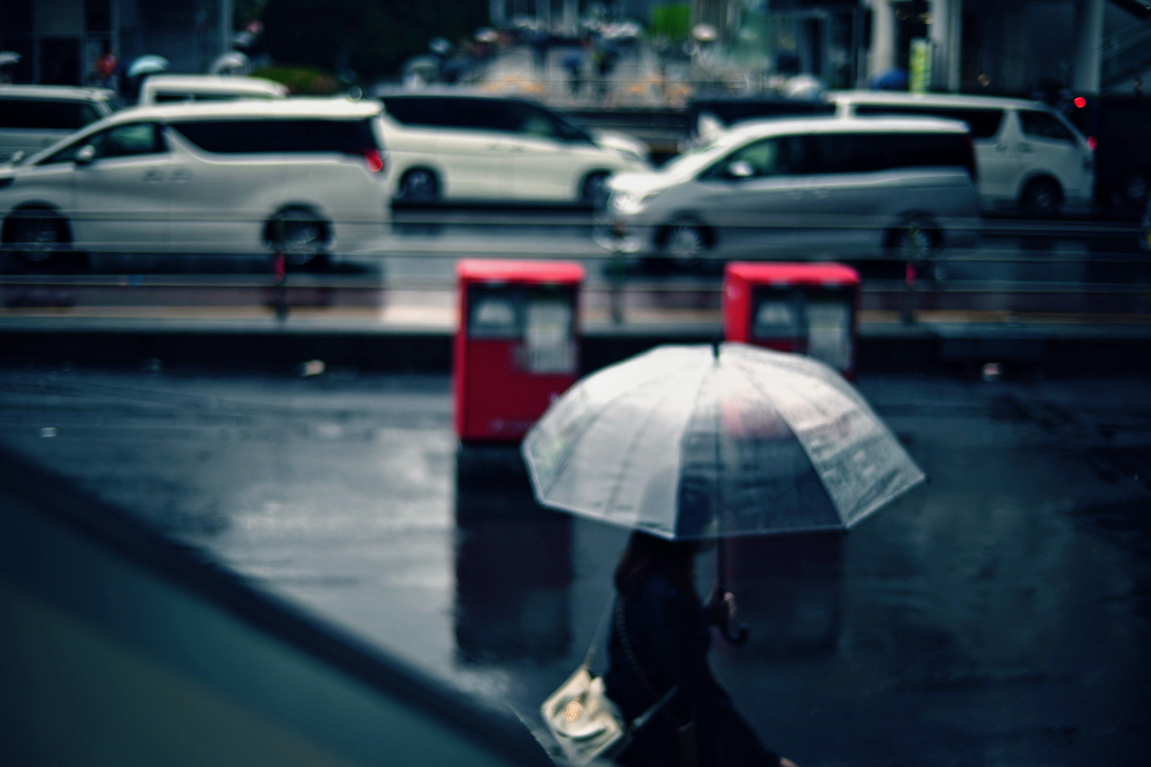 A person with an umbrella walking in the rain with white cars in the background