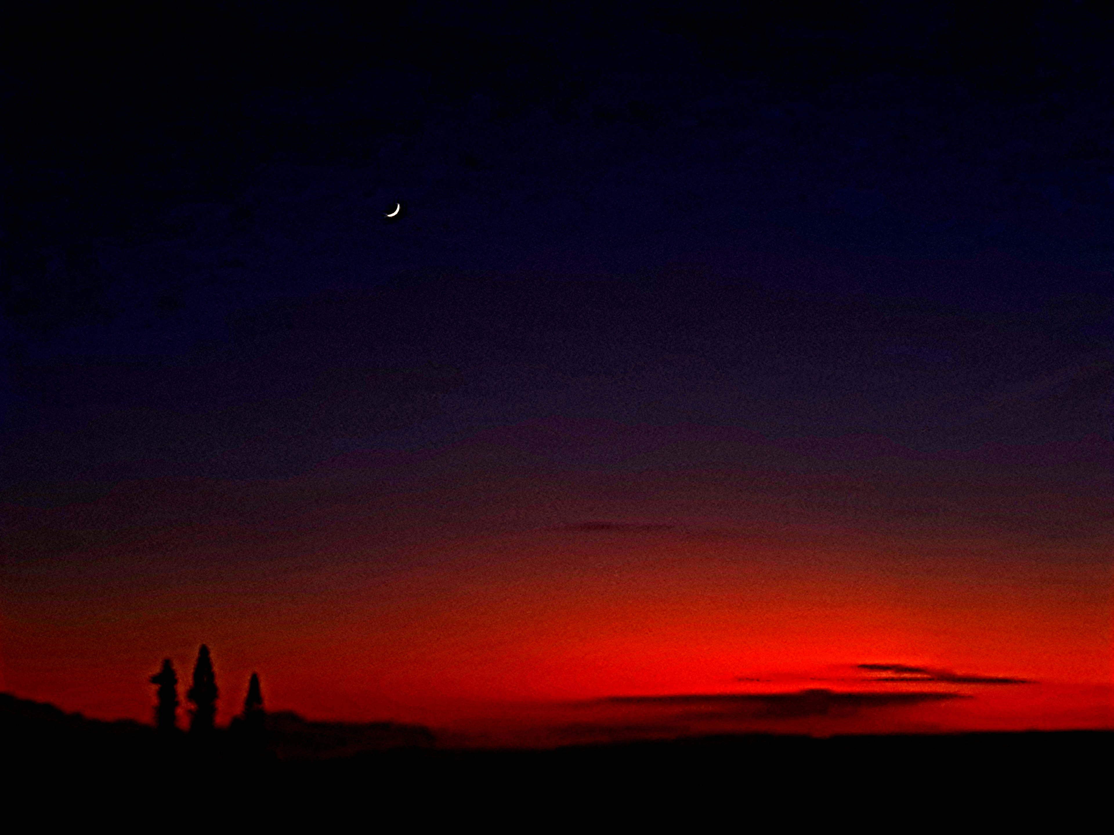 Silhouette of buildings against a sunset sky with a crescent moon