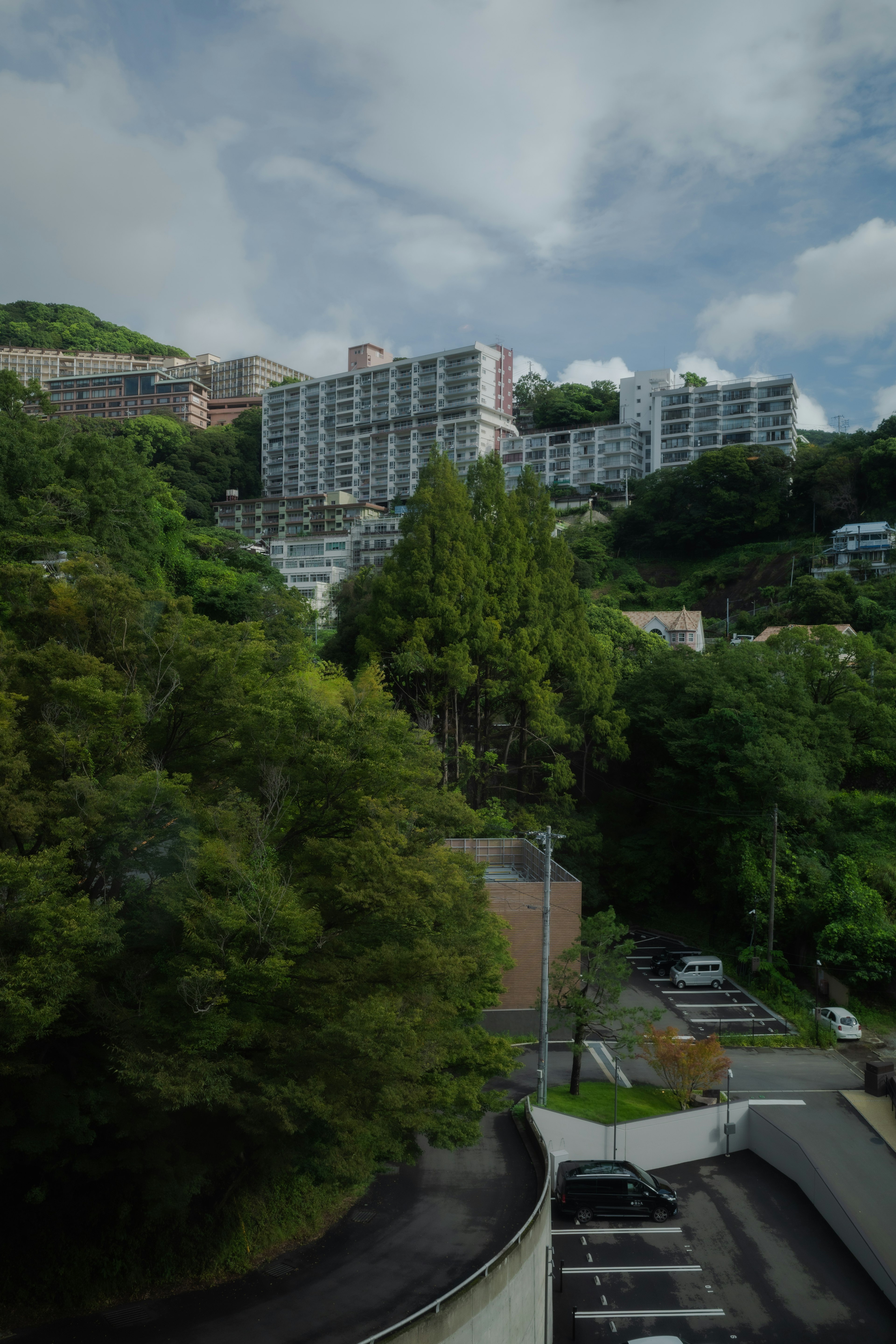 緑豊かな丘に建つ高層マンションと駐車場の風景