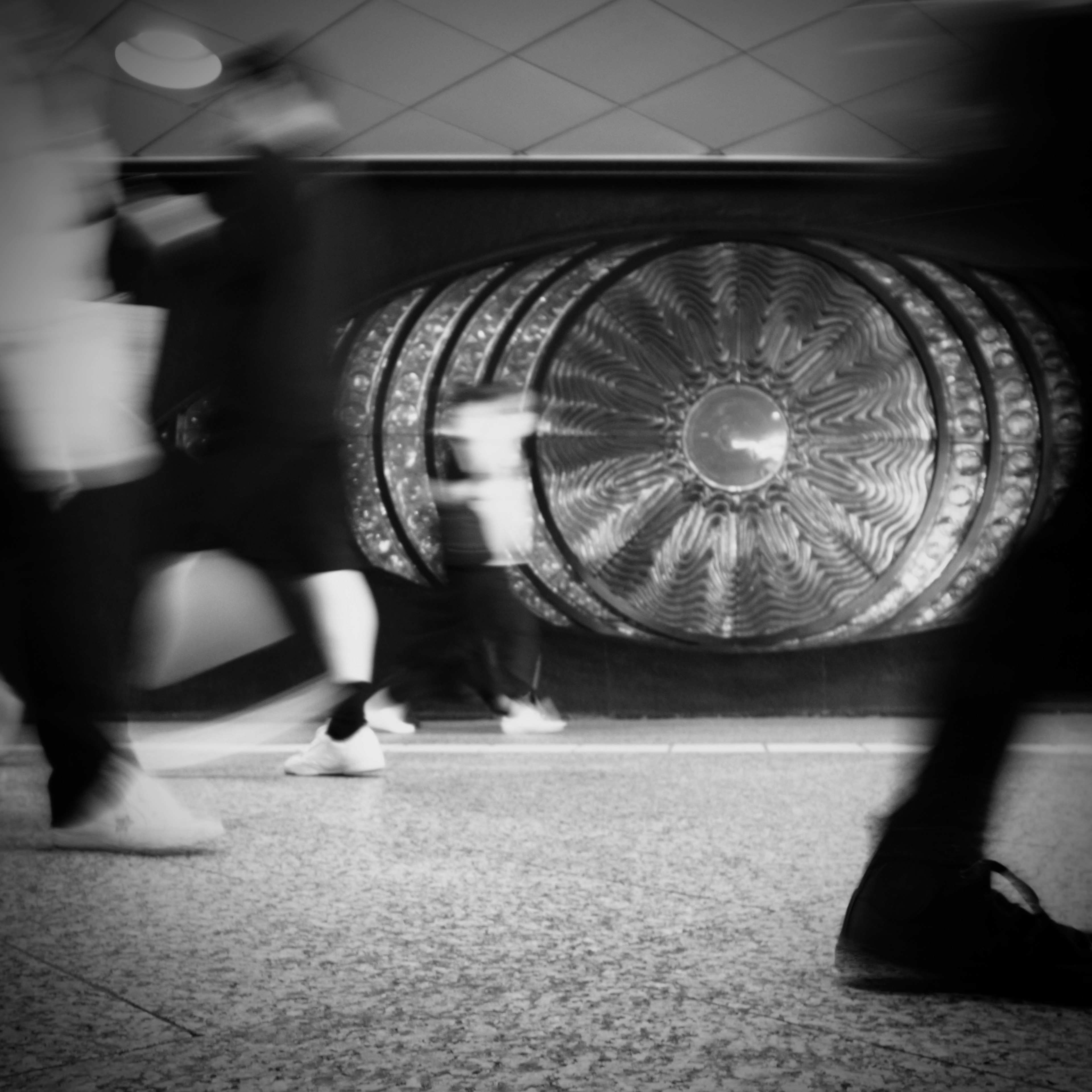 Black and white image of moving people in a subway station with decorative wall art