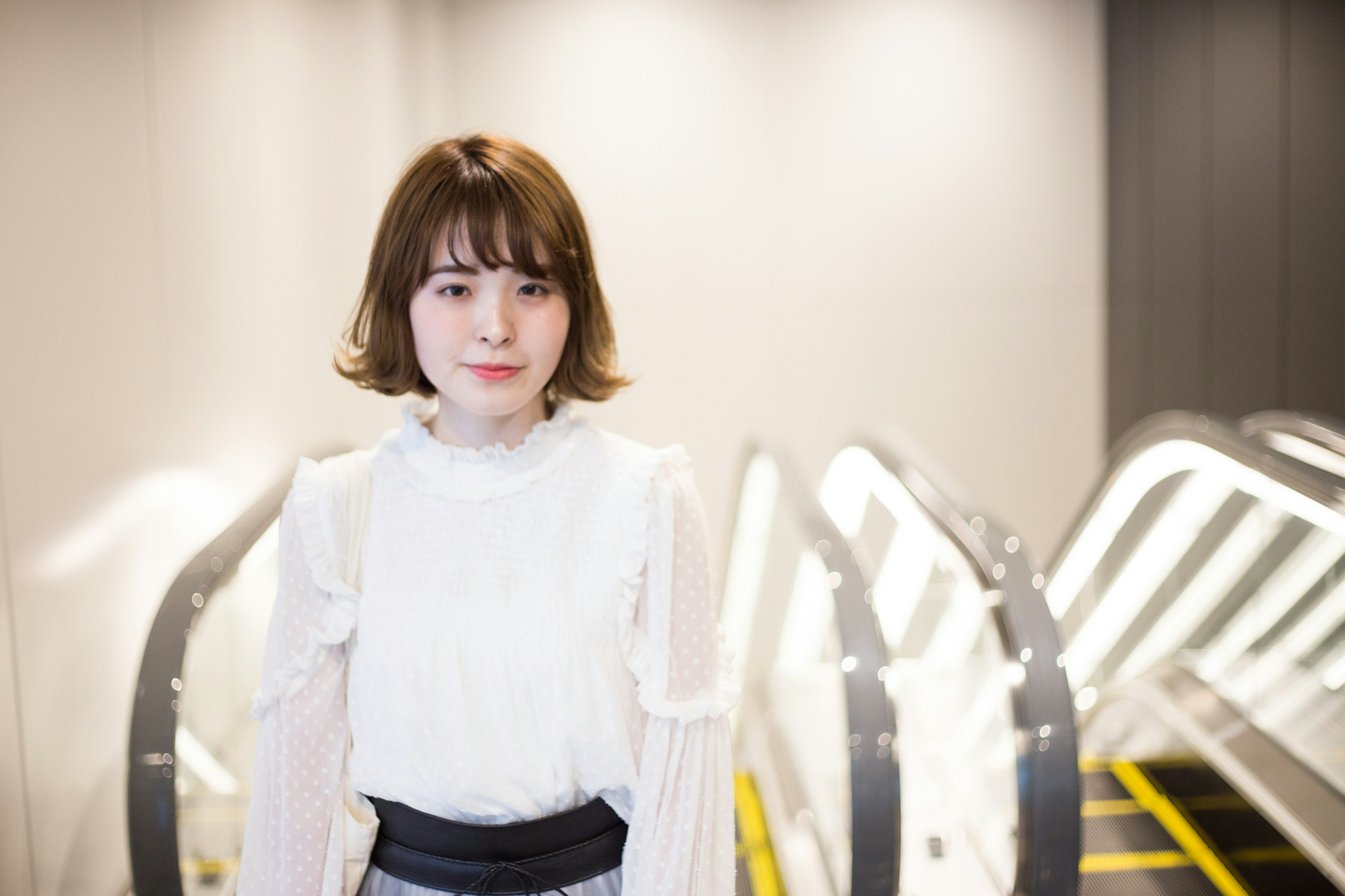 A woman in a white blouse standing in front of an escalator