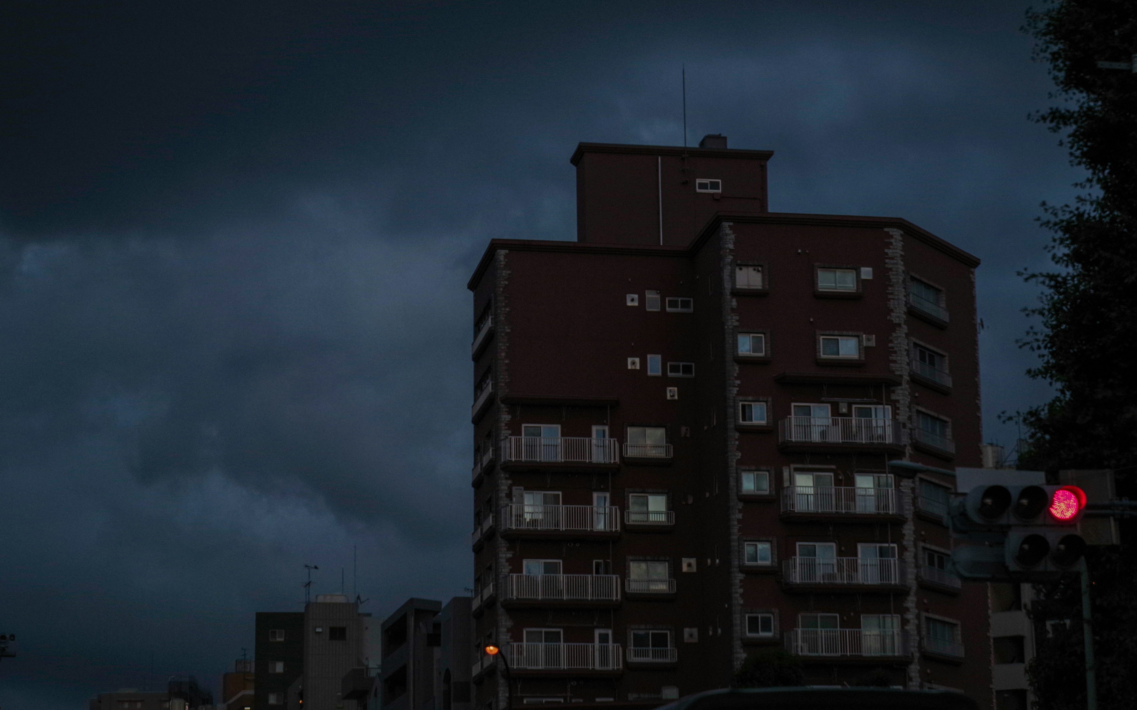 Urban landscape under dark clouds featuring a high-rise building and a red traffic light