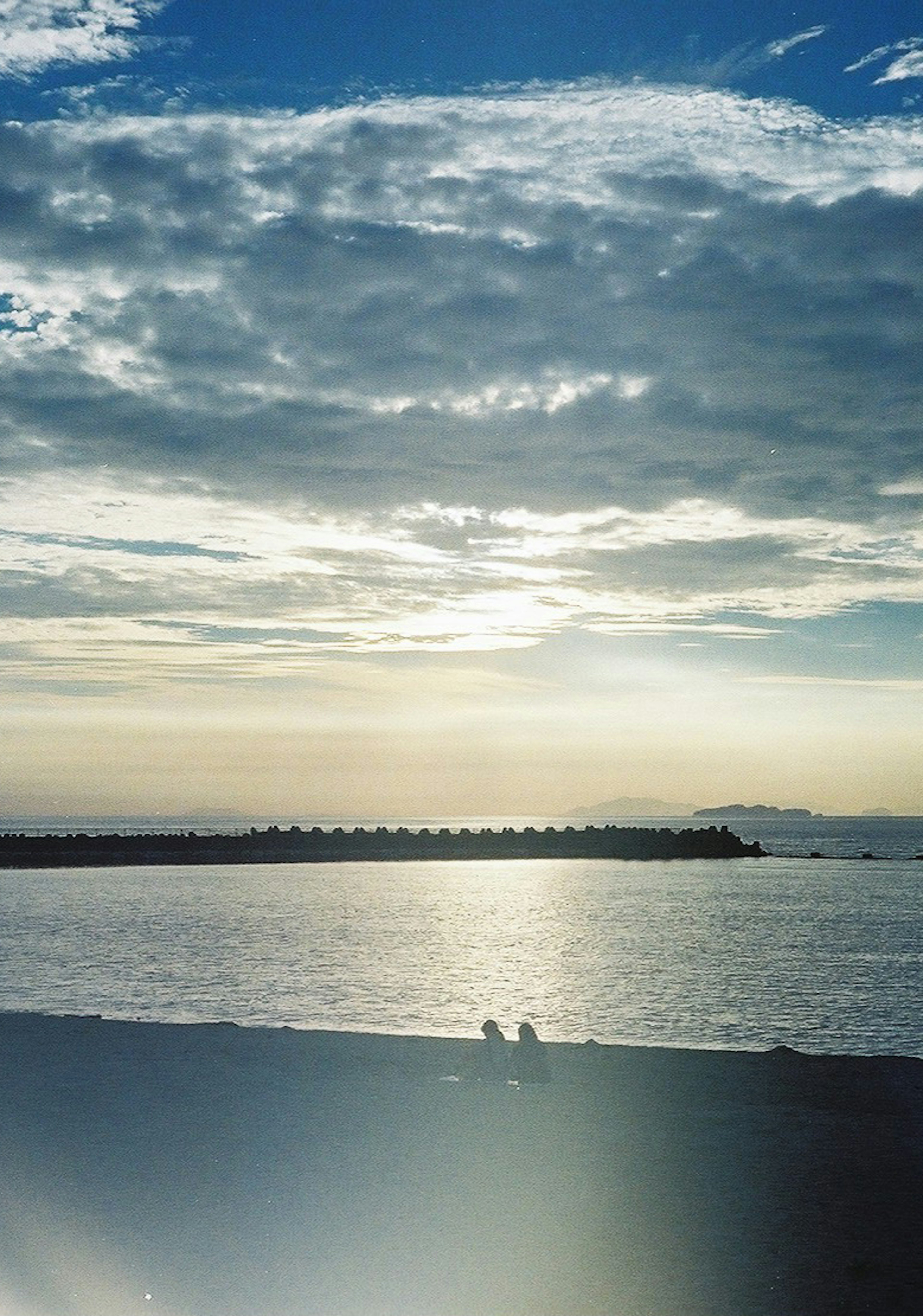 夕日を背景にした海岸で二人の人が座っている風景