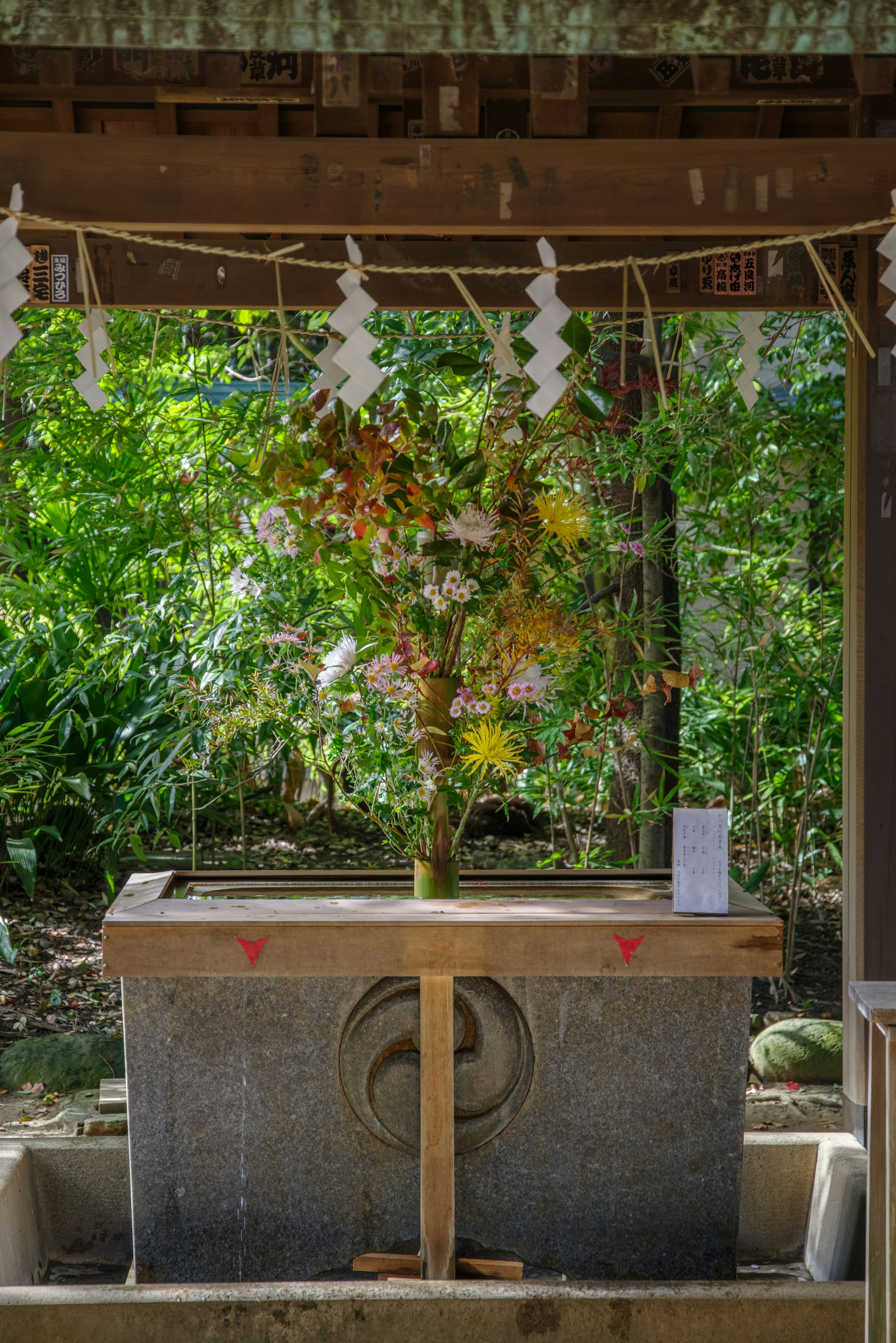 Stone water basin at a shrine with floral decorations and lush greenery