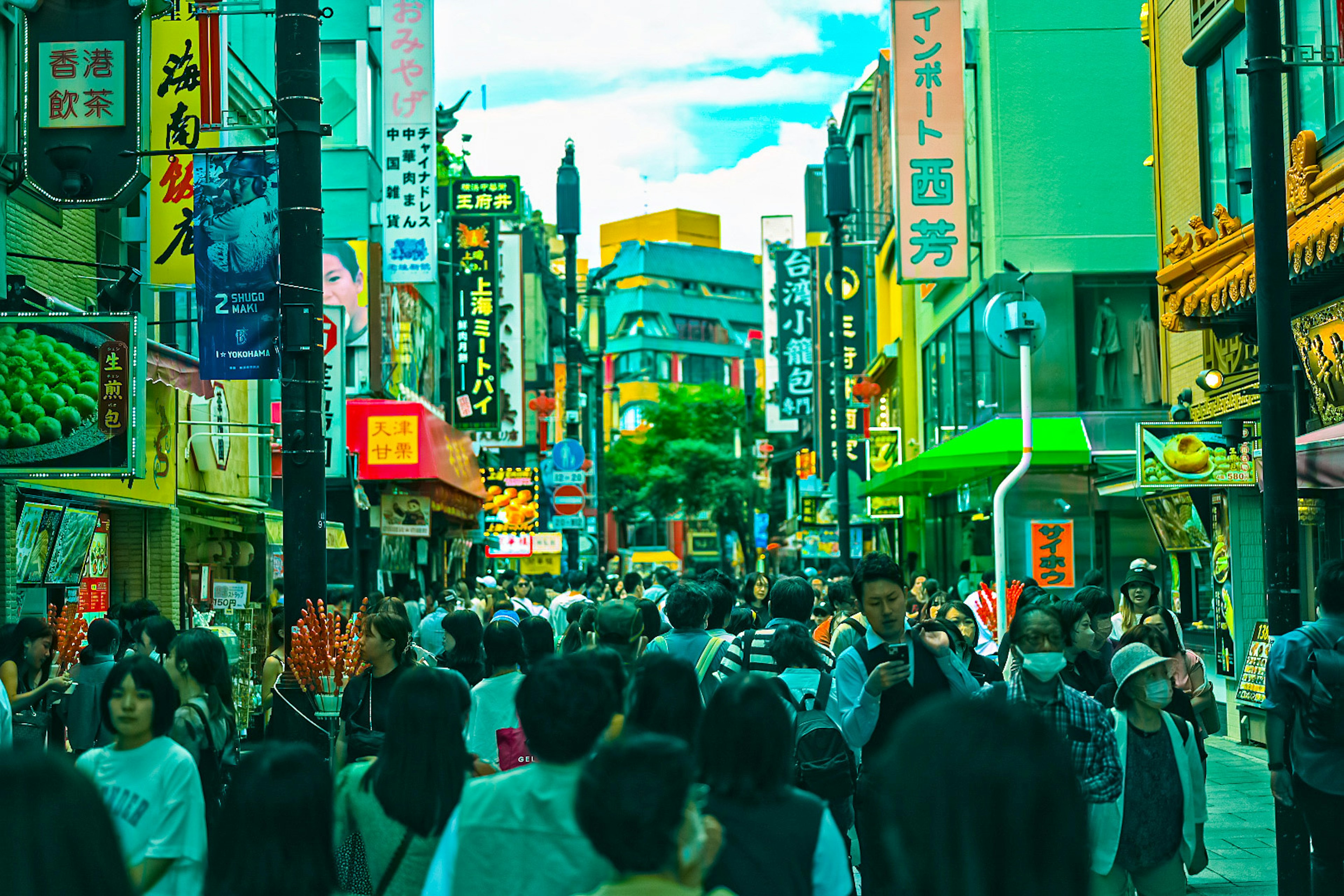 Bustling street scene with crowds of people colorful signs and a bright blue sky