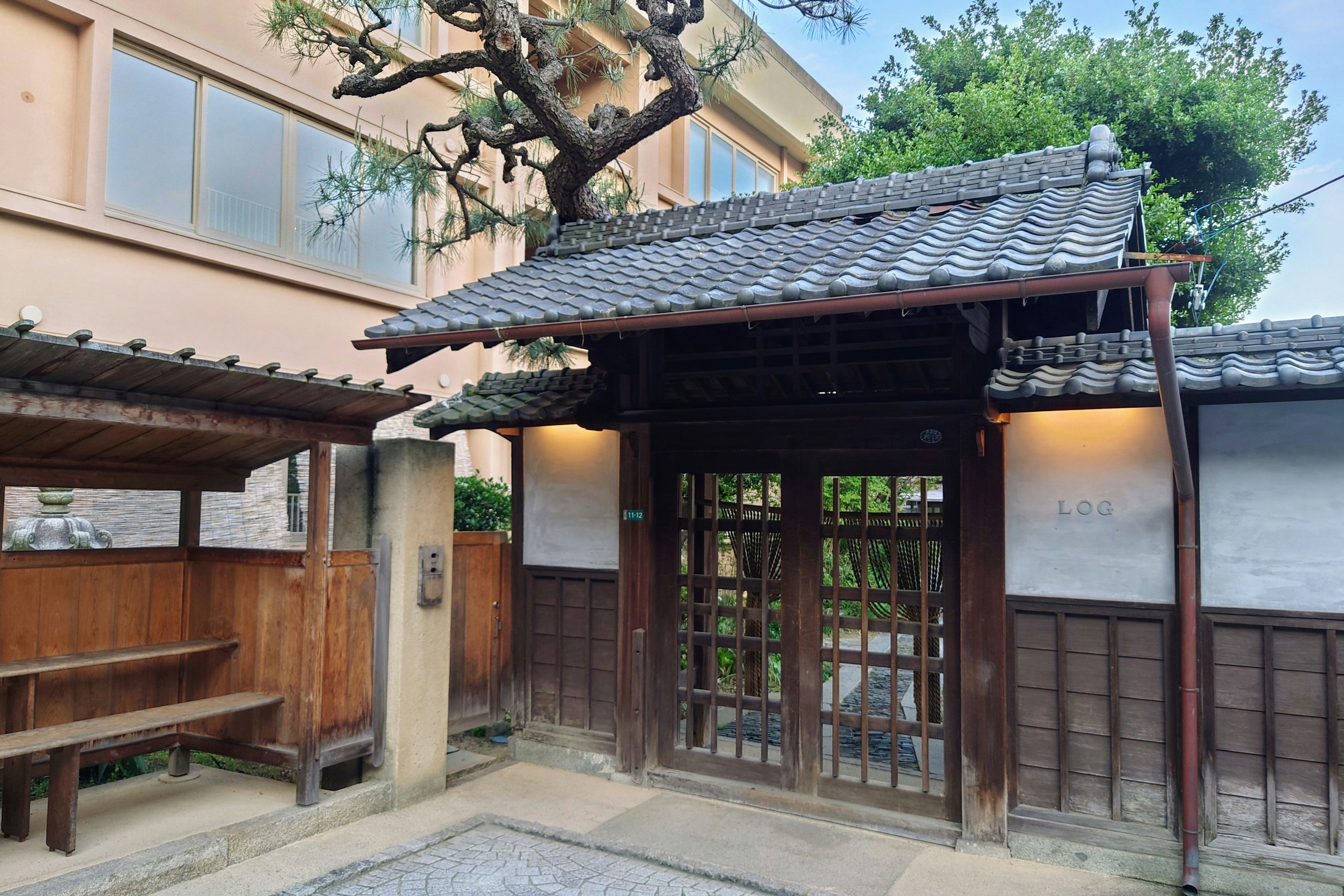 Entrée d'une maison japonaise traditionnelle avec porte en bois et toit en tuiles entourée de verdure