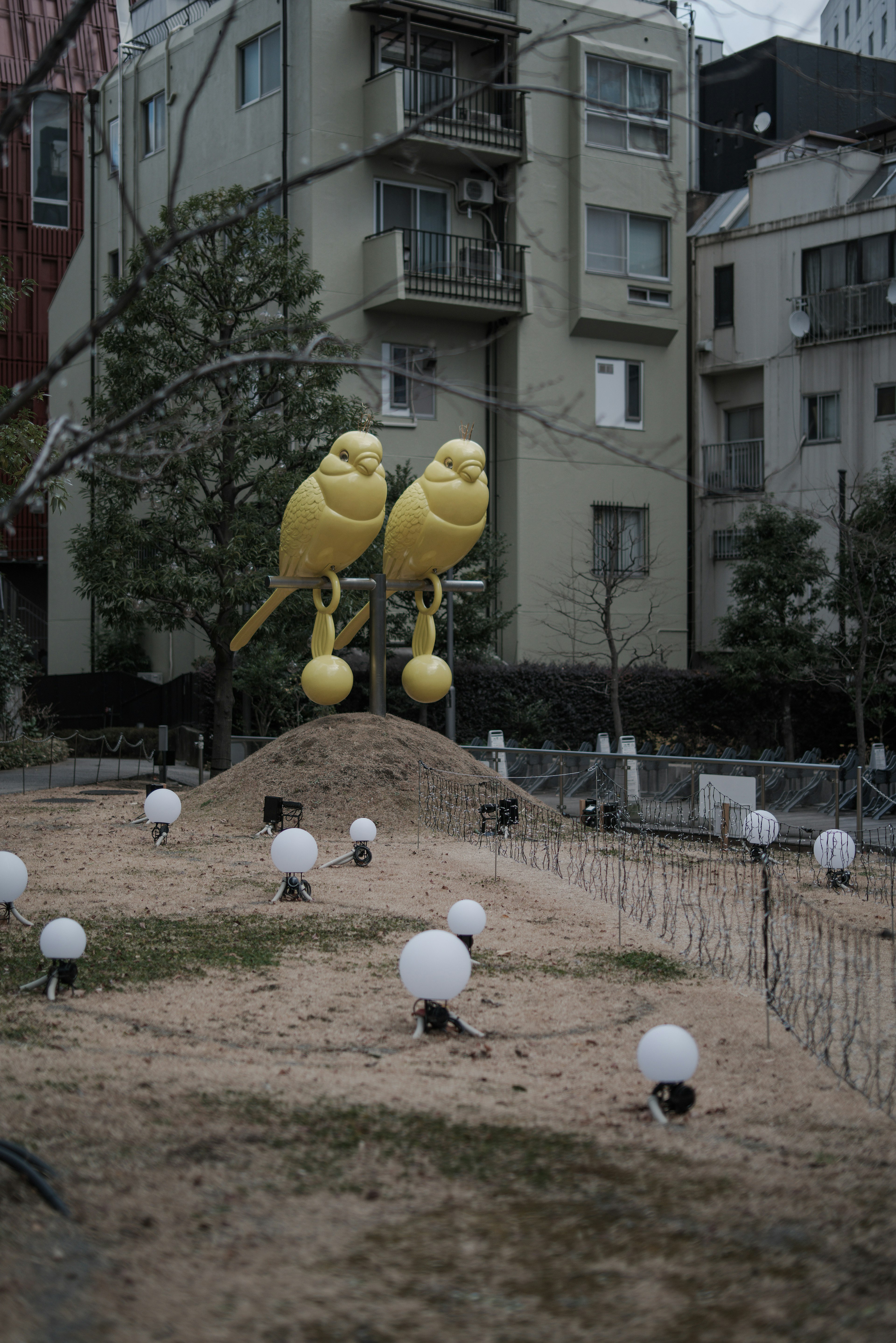 Large yellow bird sculptures in a park surrounded by white spherical lights