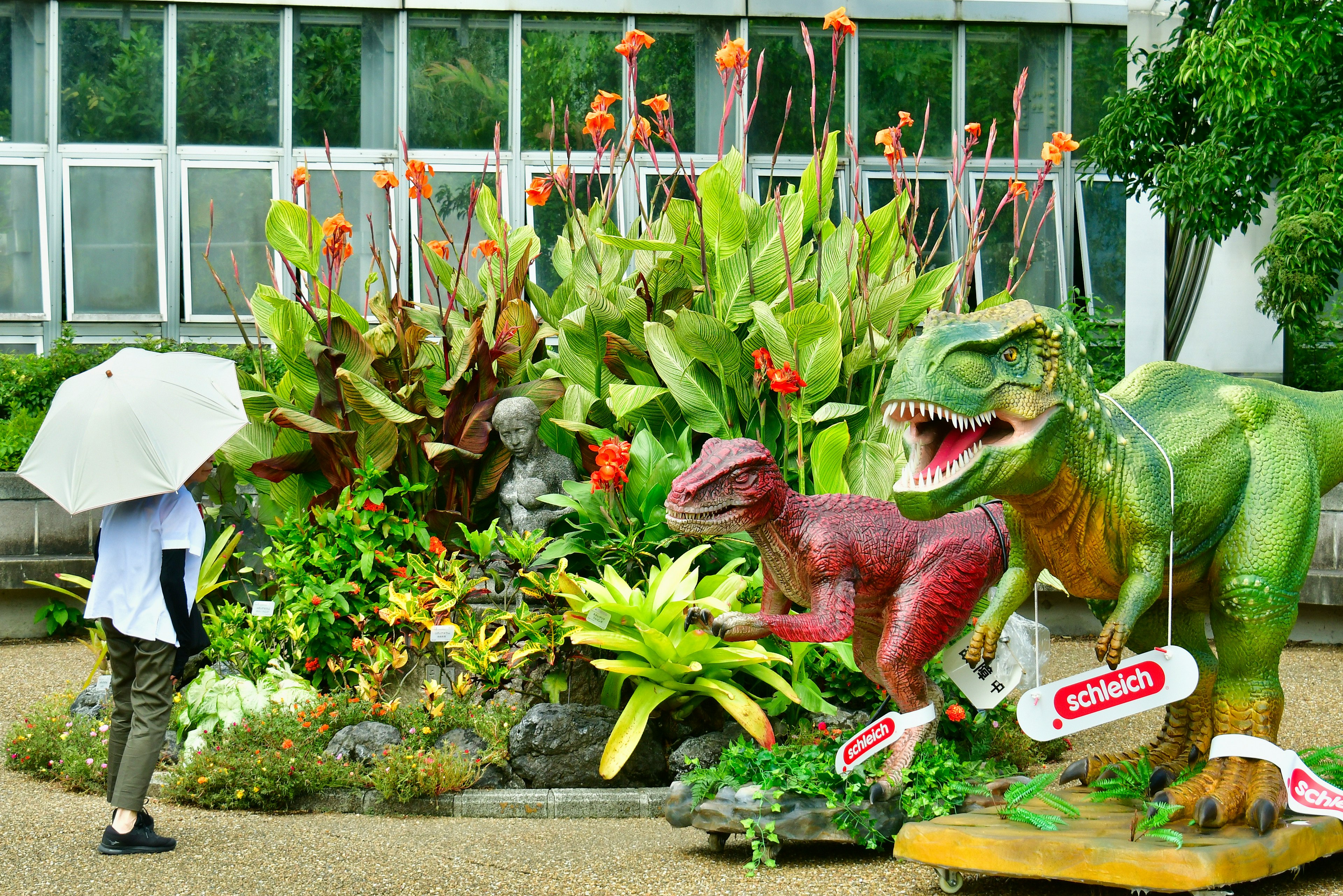 Ein lebendiger Garten mit Dinosaurierskulpturen und einer Person mit einem Regenschirm