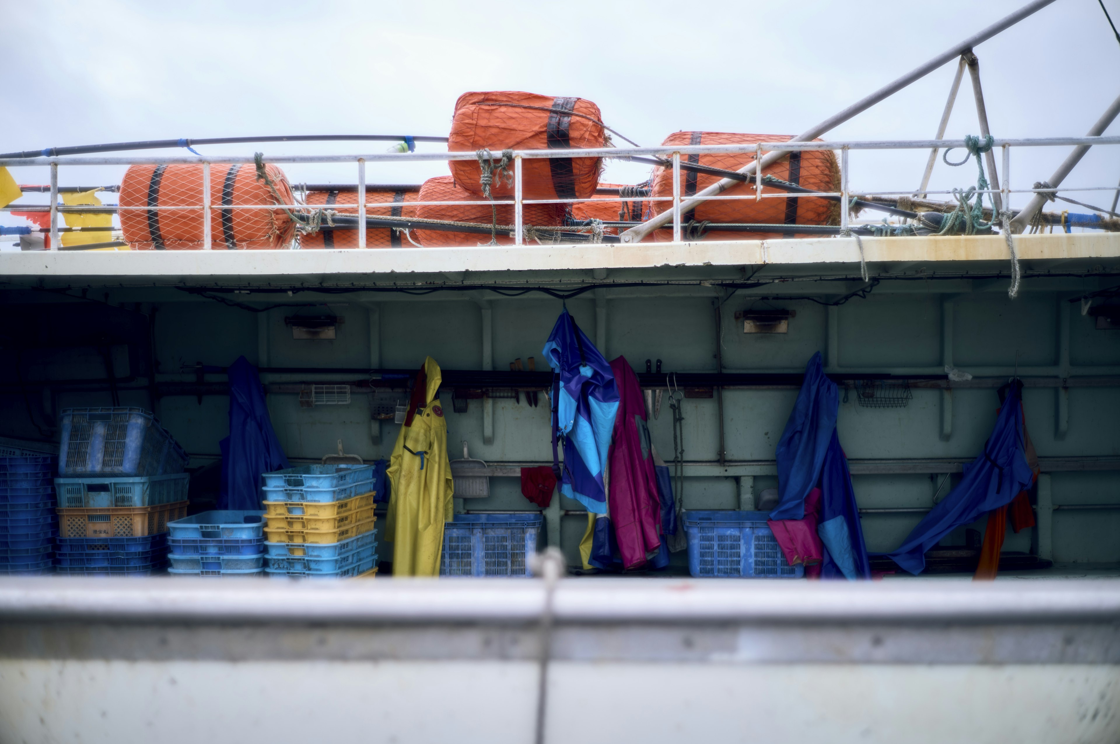 Colorful fishing gear and containers on a boat deck with orange life buoys