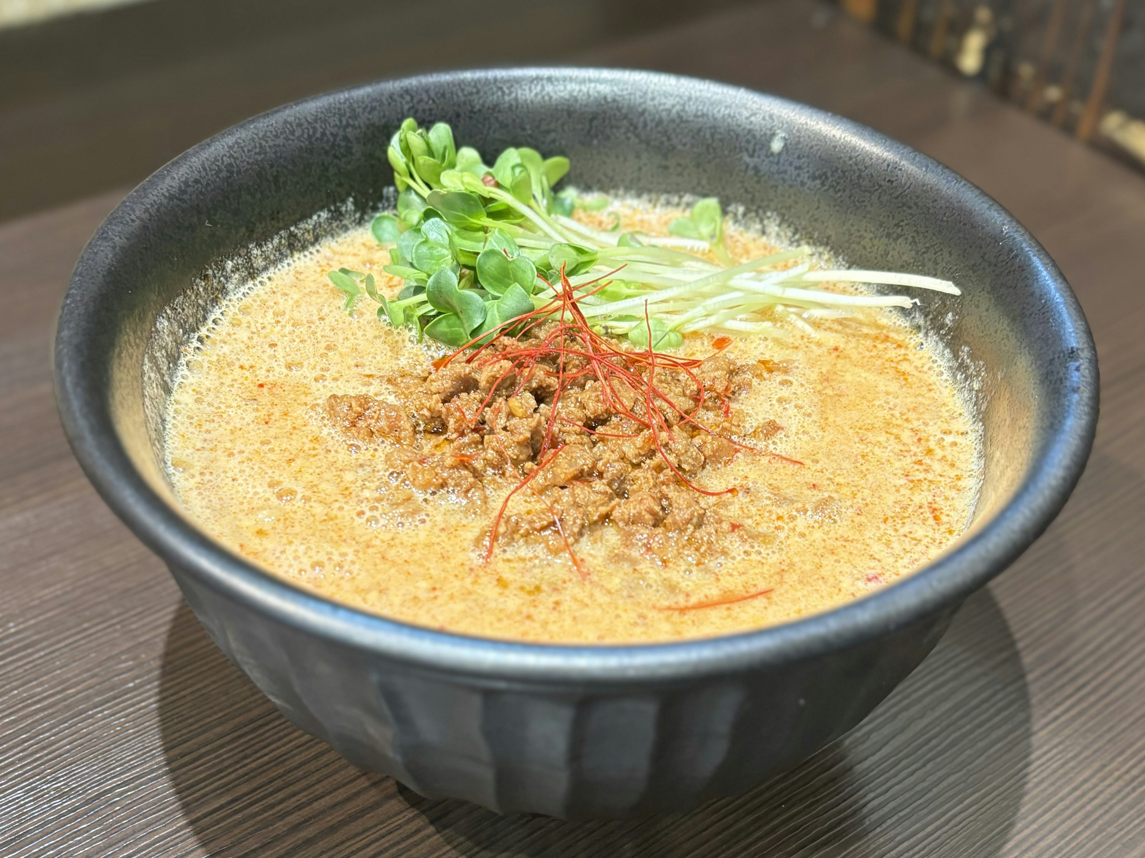 Creamy ramen served in a black bowl topped with herbs and minced meat