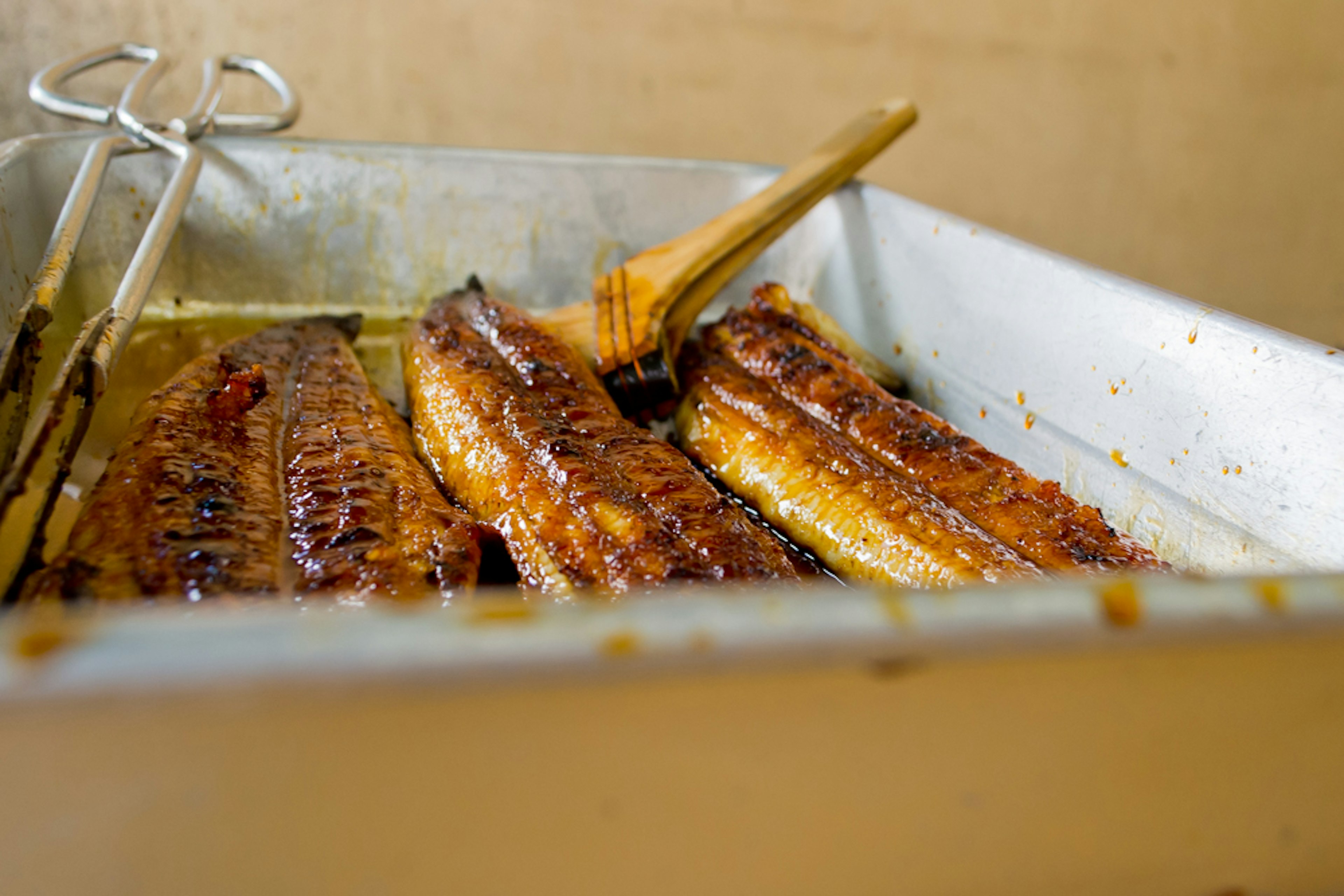 Filetes de anguila a la parrilla brillando en una bandeja con una espátula de madera