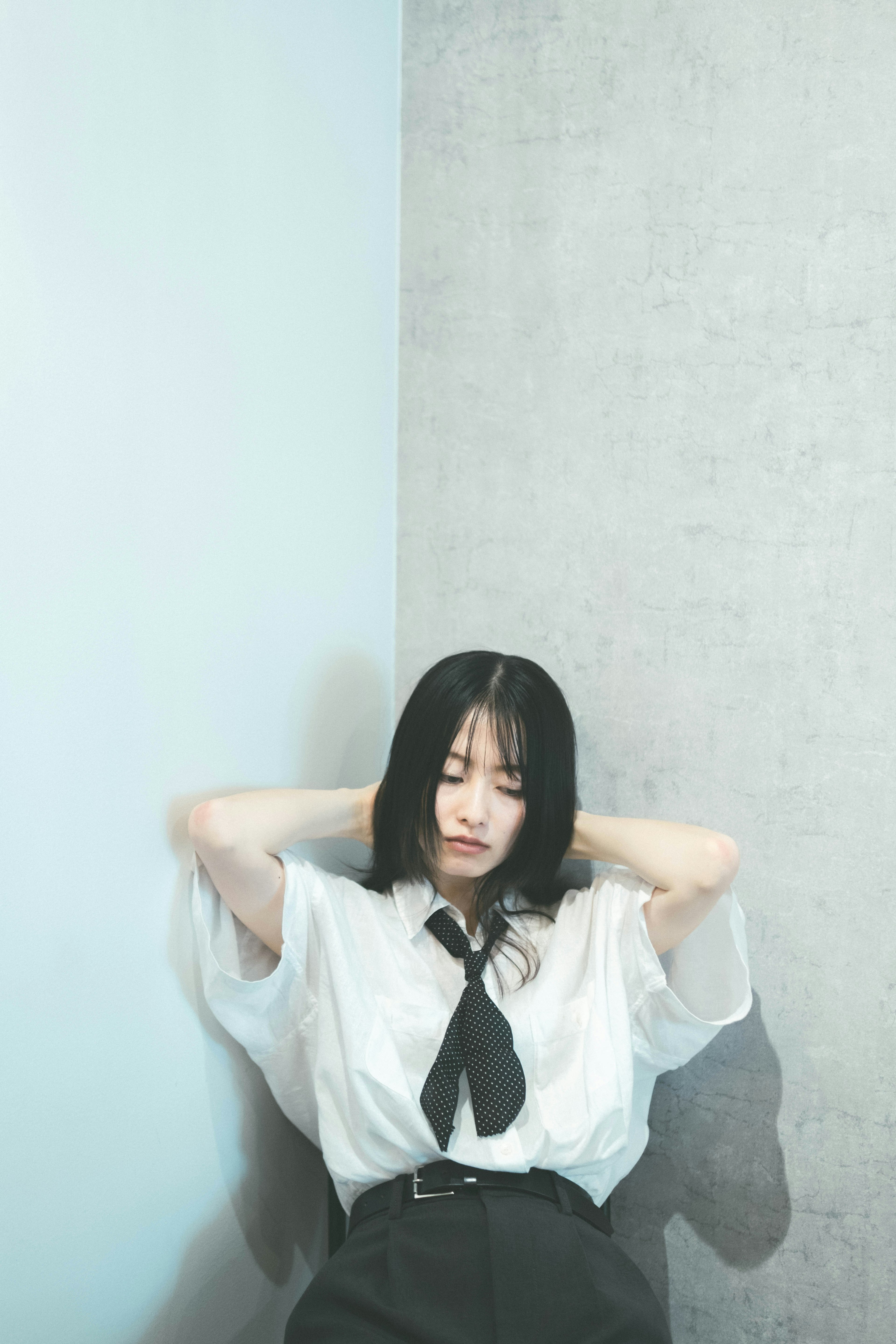 Young woman leaning against a gray wall wearing a white shirt and black skirt