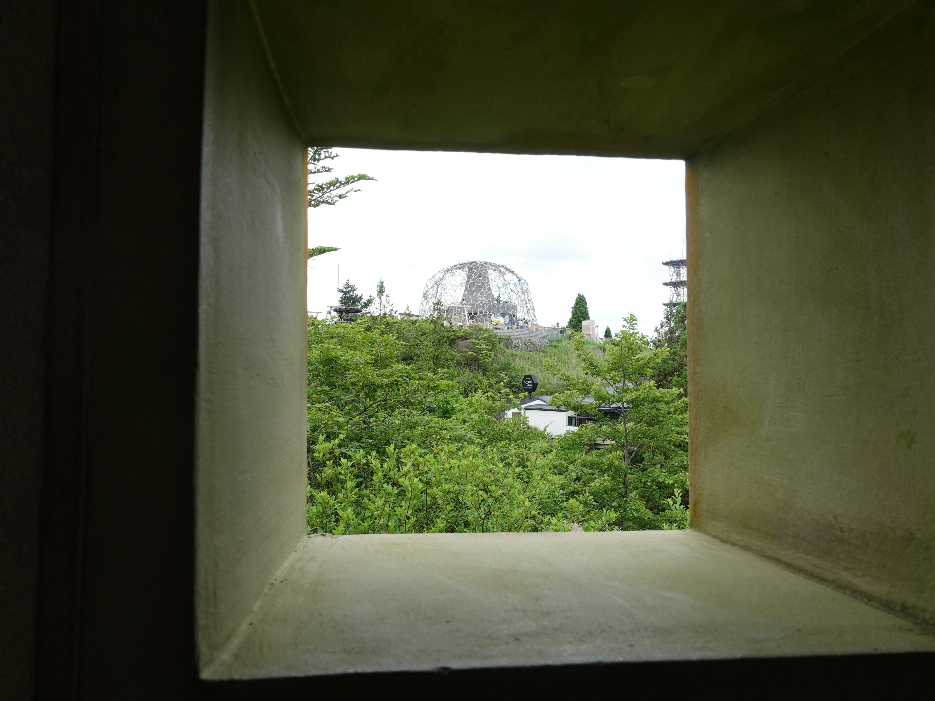 Vue depuis une fenêtre montrant un paysage verdoyant et une structure en forme de dôme